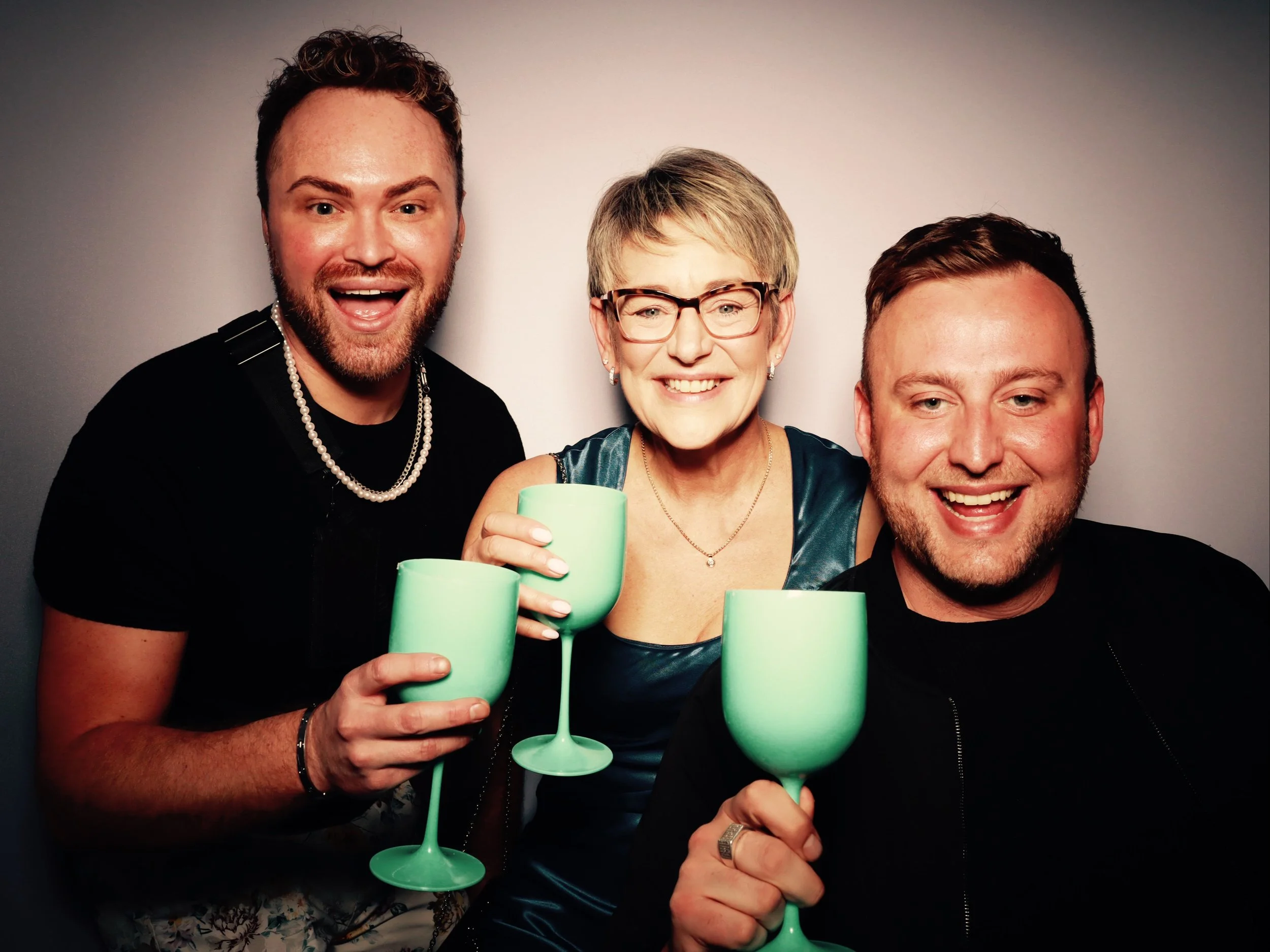 Three smiling people holding green glasses, two men and one woman, celebrating together.