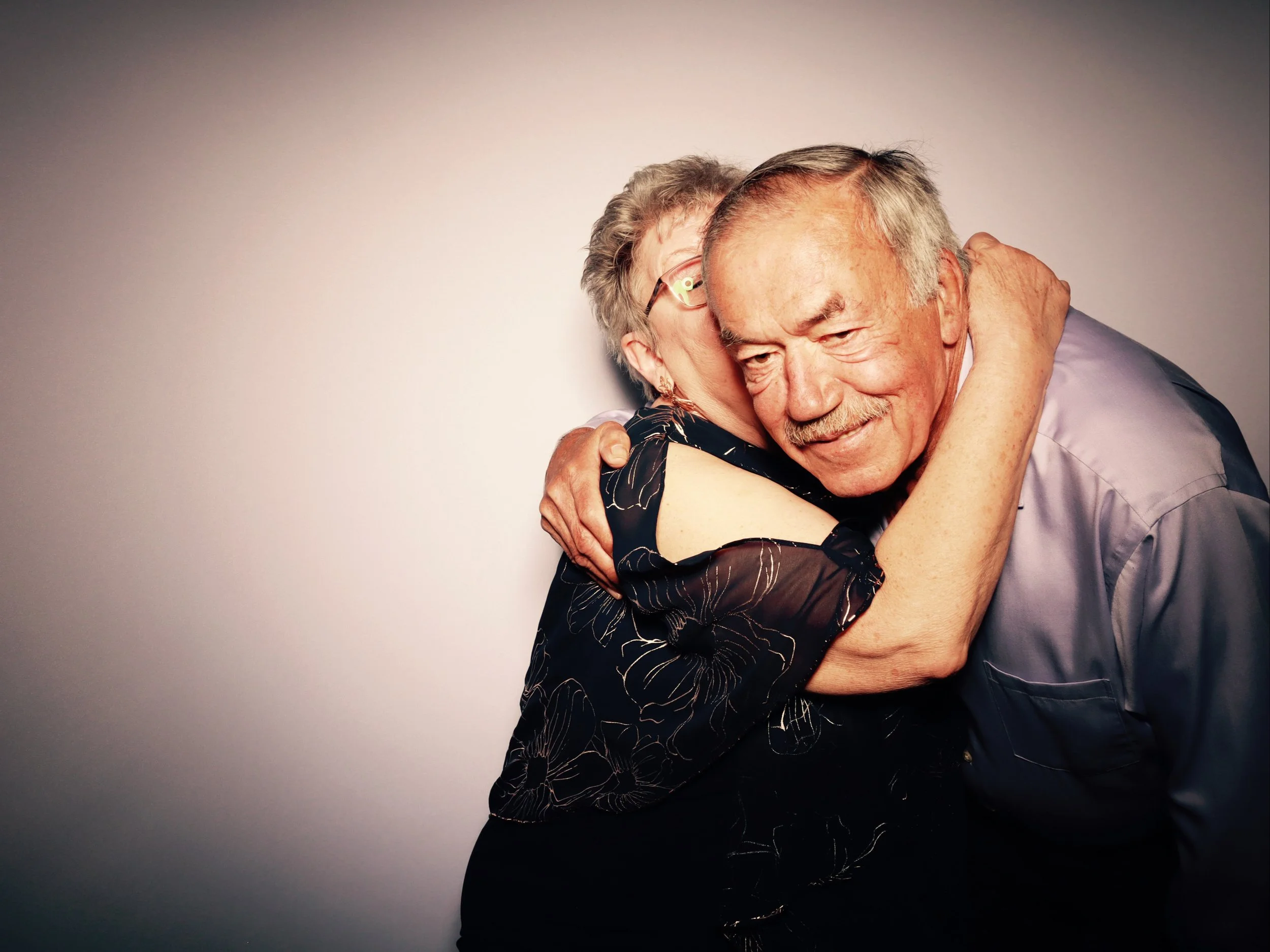 An elderly couple hugging each other warmly, smiling and showing affection.