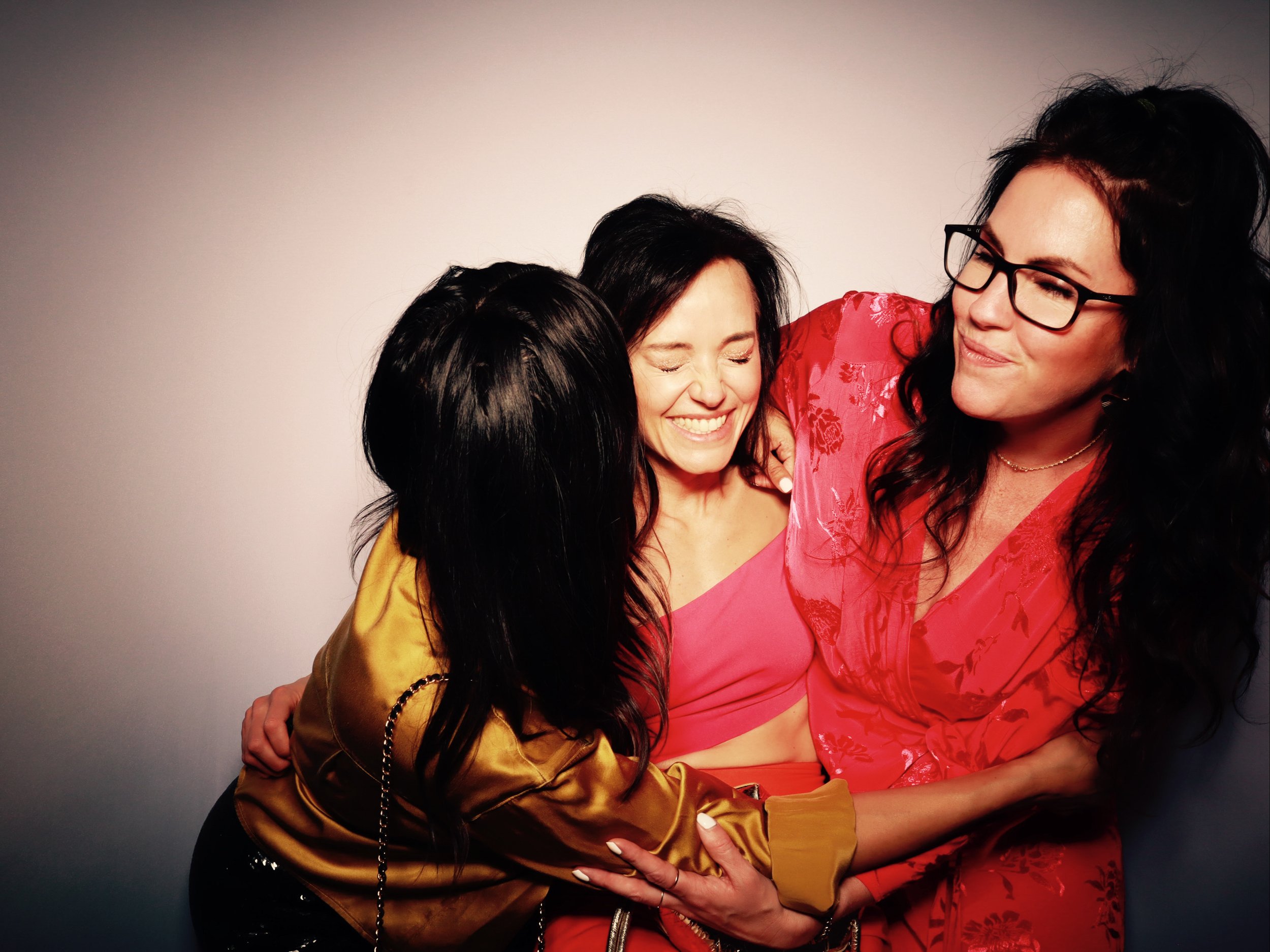 Three women in colorful clothing sharing a joyful embrace, smiling and laughing together.