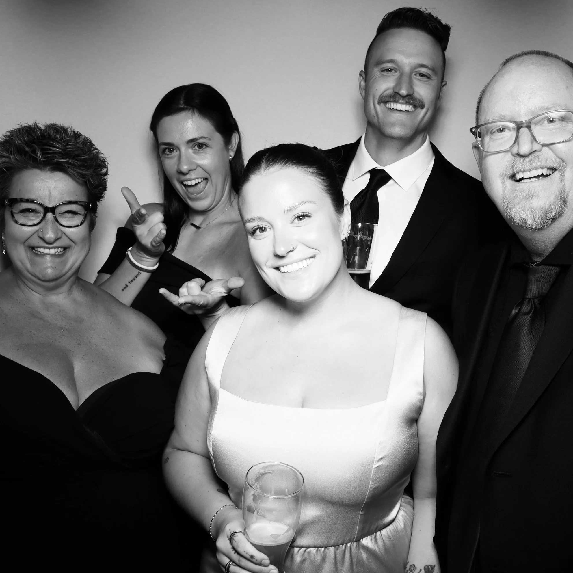 Group of six people at a celebration, smiling and posing together, with one holding a drink, in black and white.