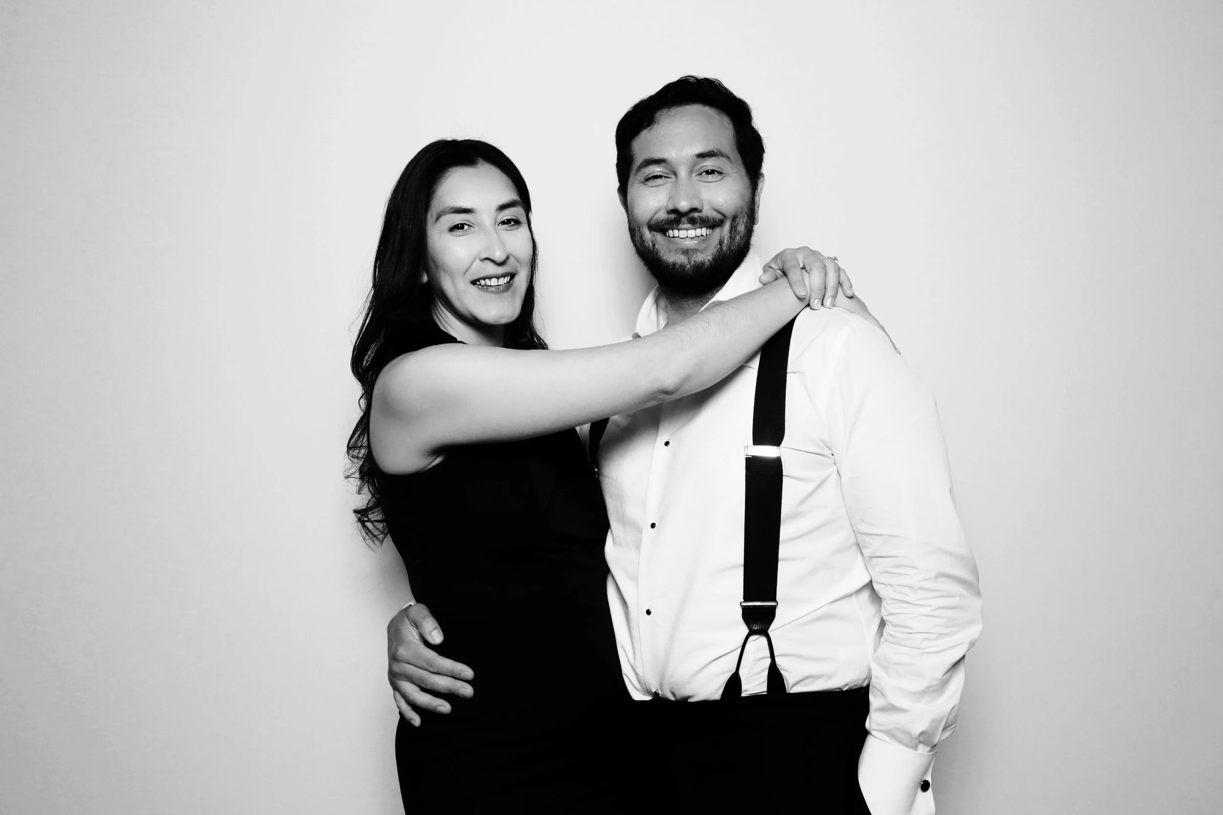 A smiling man and woman embracing against a plain background, black and white photo
