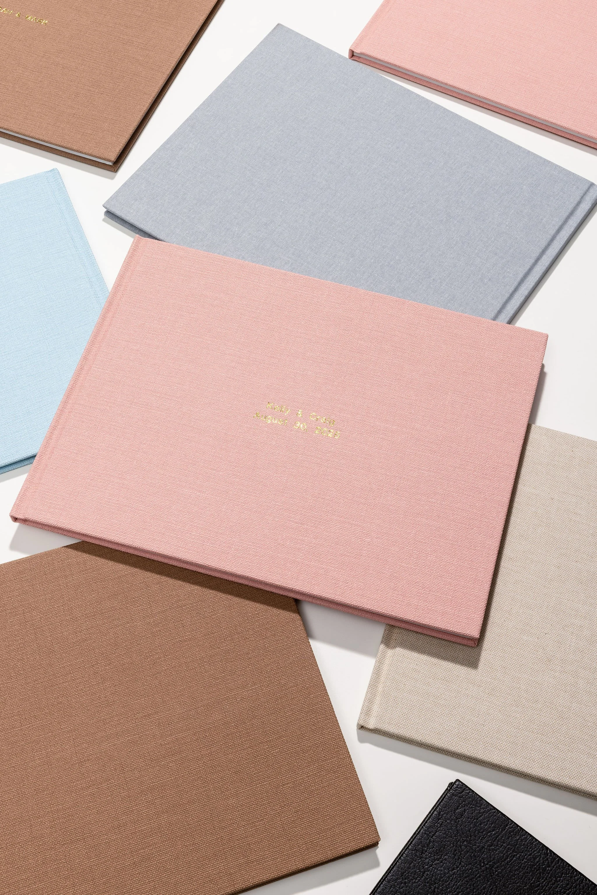 Multiple fabric-covered photo albums in pastel colors, one with gold embossed text, displayed on a white surface.