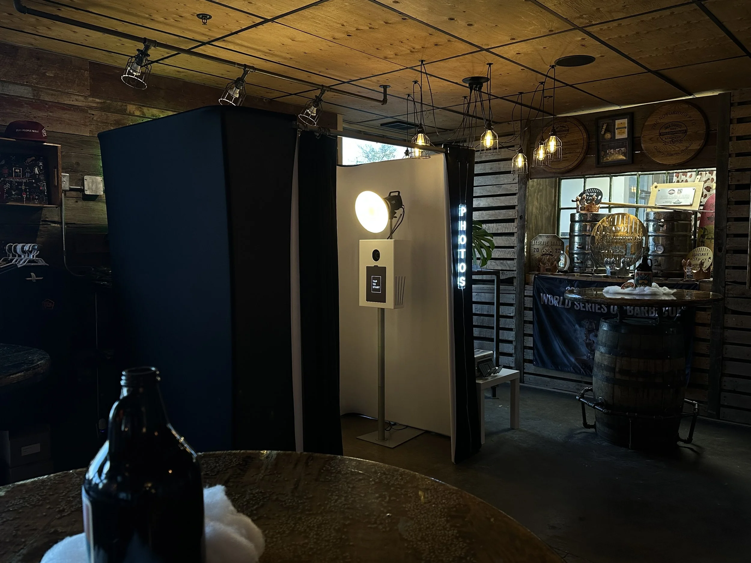 Photo booth setup with a photo frame, lighting, and signage in a bar or restaurant decorated with wooden panels and beer-themed decor.