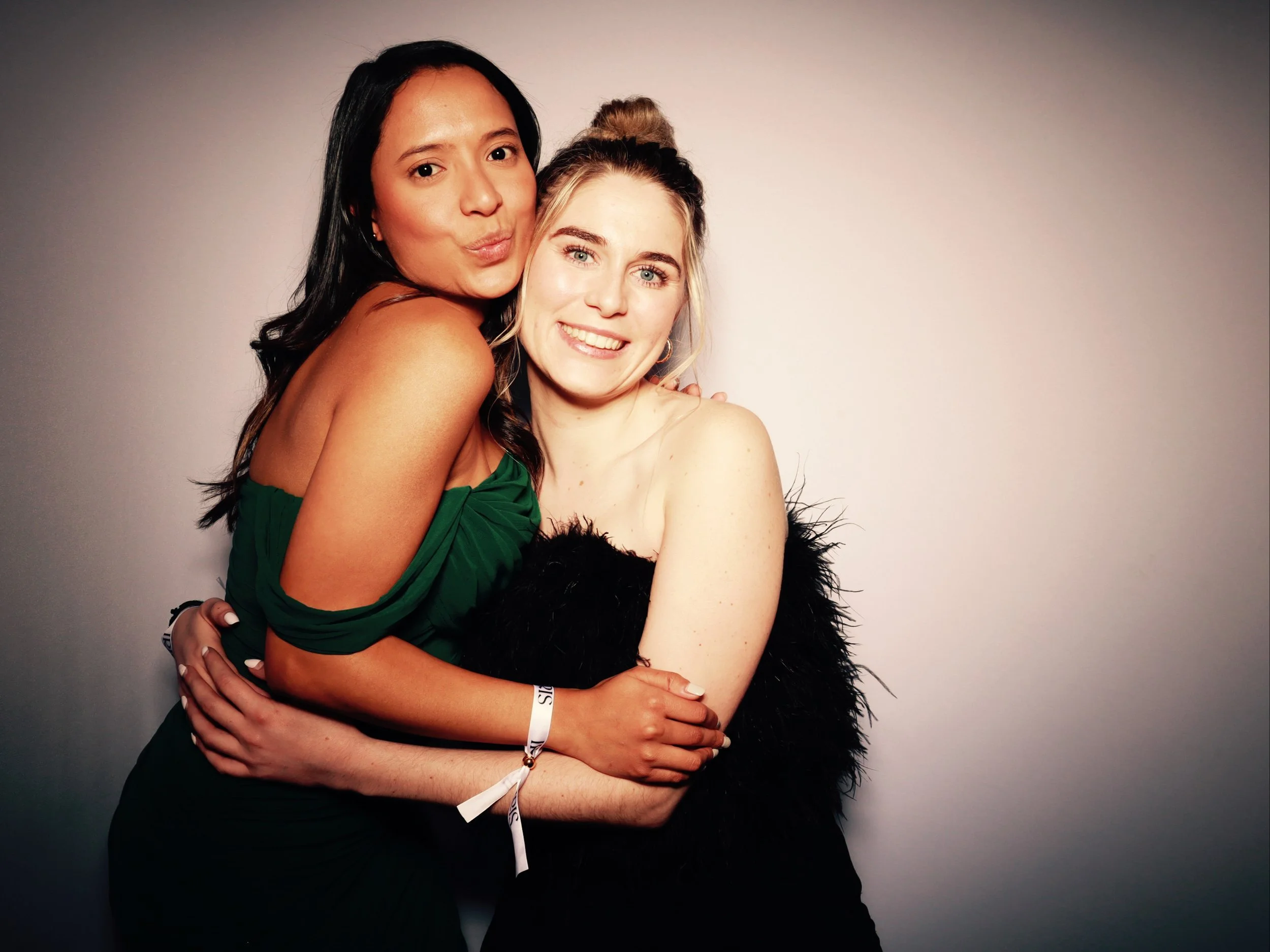 Two women hugging and smiling at the camera against a plain background.