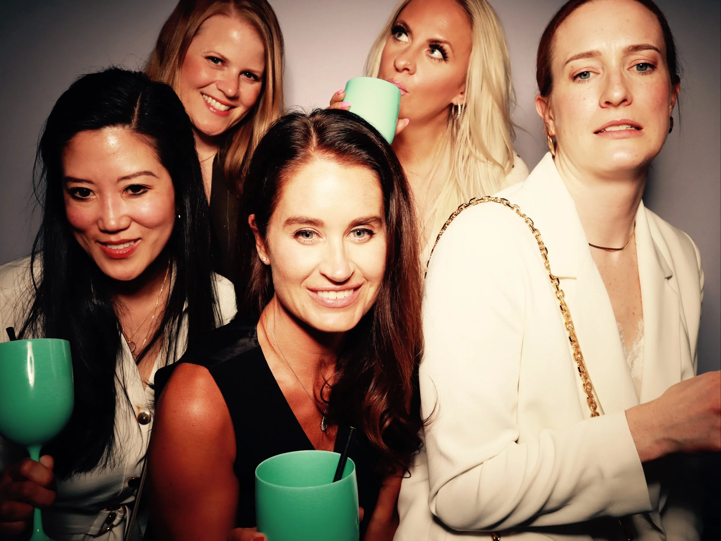 Group of five diverse women at a social gathering, some holding green cups, posing and smiling in a close-up photo.