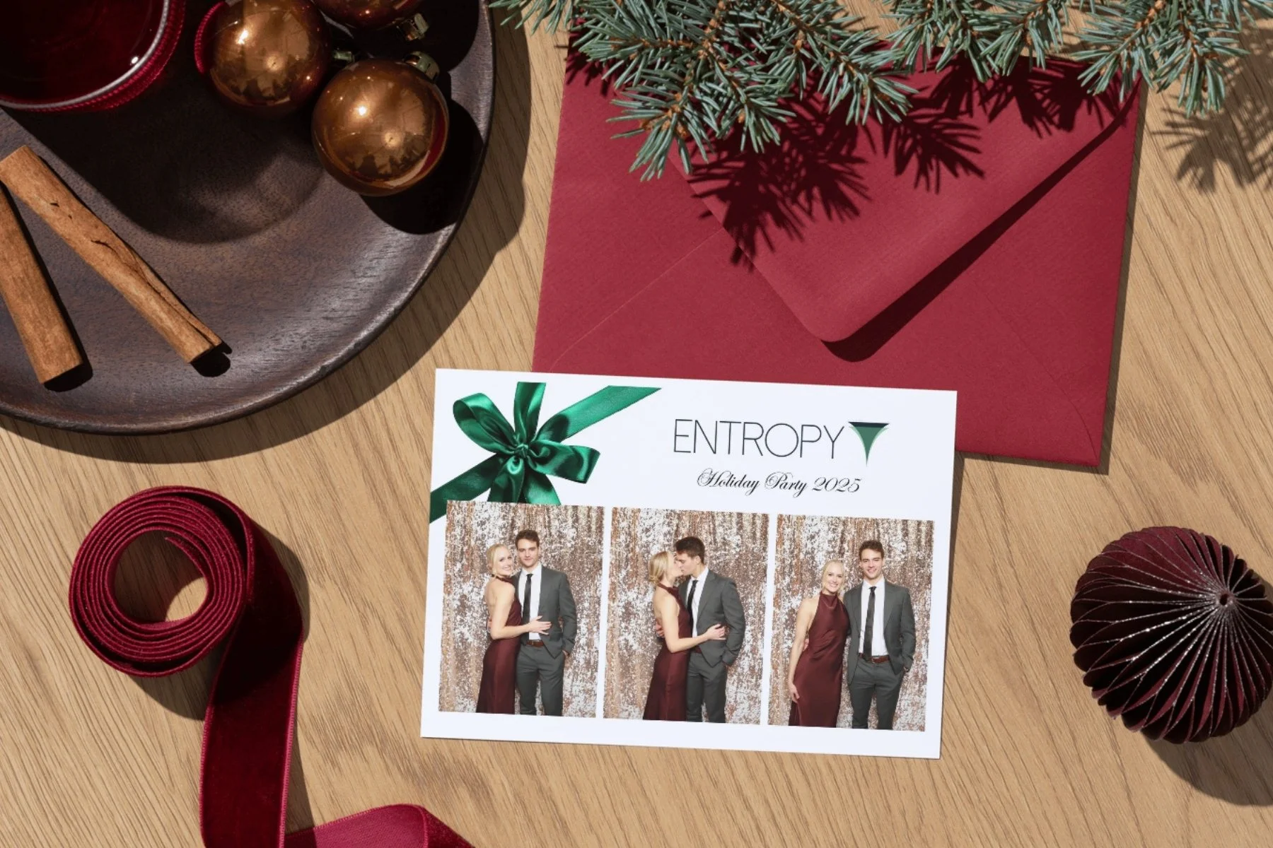 Photo of a holiday party invitation card titled 'ENTROPY Holiday Party 2025' with images of four people in formal attire, surrounded by Christmas decorations including a pine branch, red envelope, red ribbon, cinnamon sticks, gold ornaments, and a folded red spiral paper ornament.