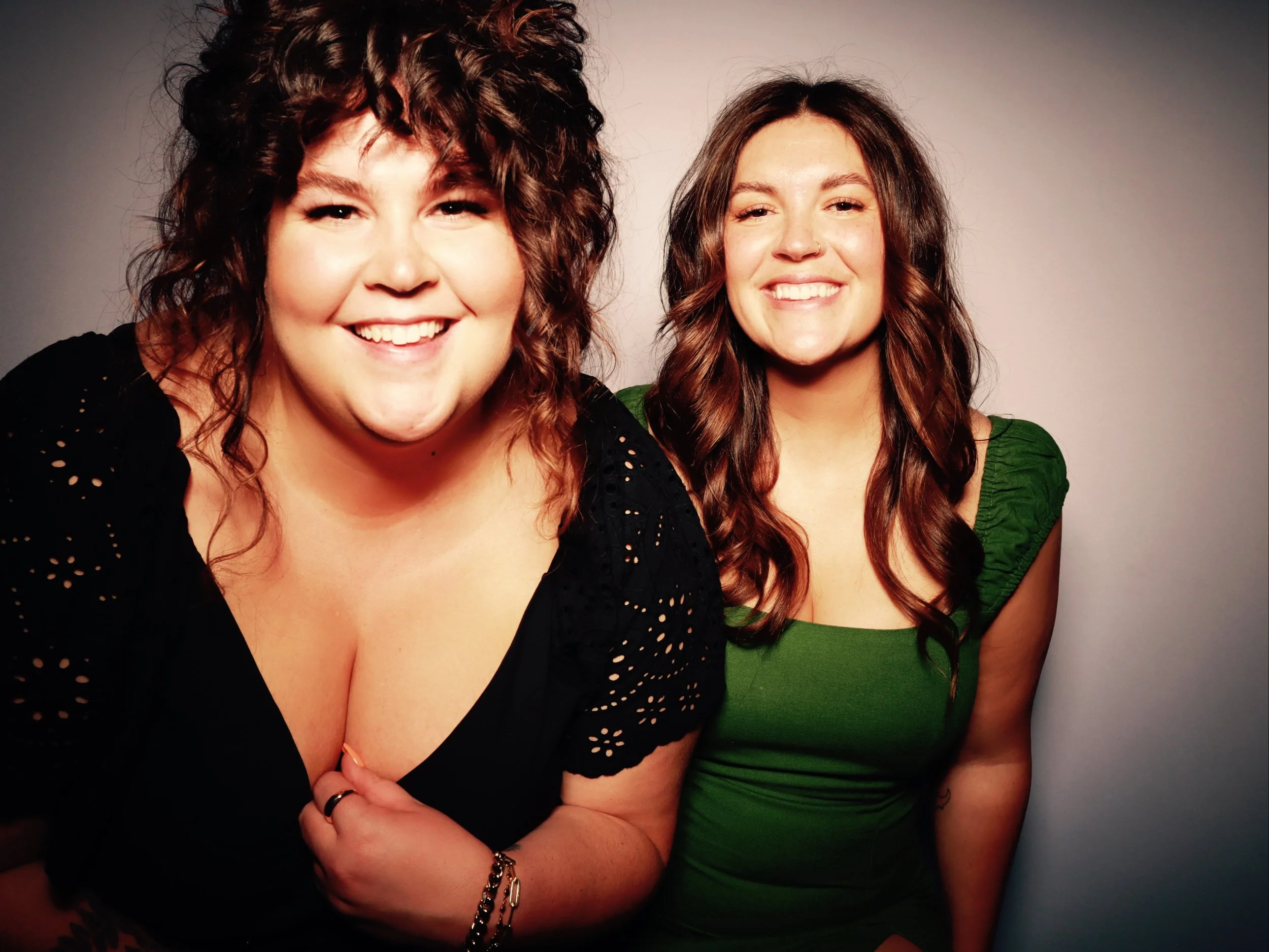 Two smiling women with brown hair posing together against a plain background.