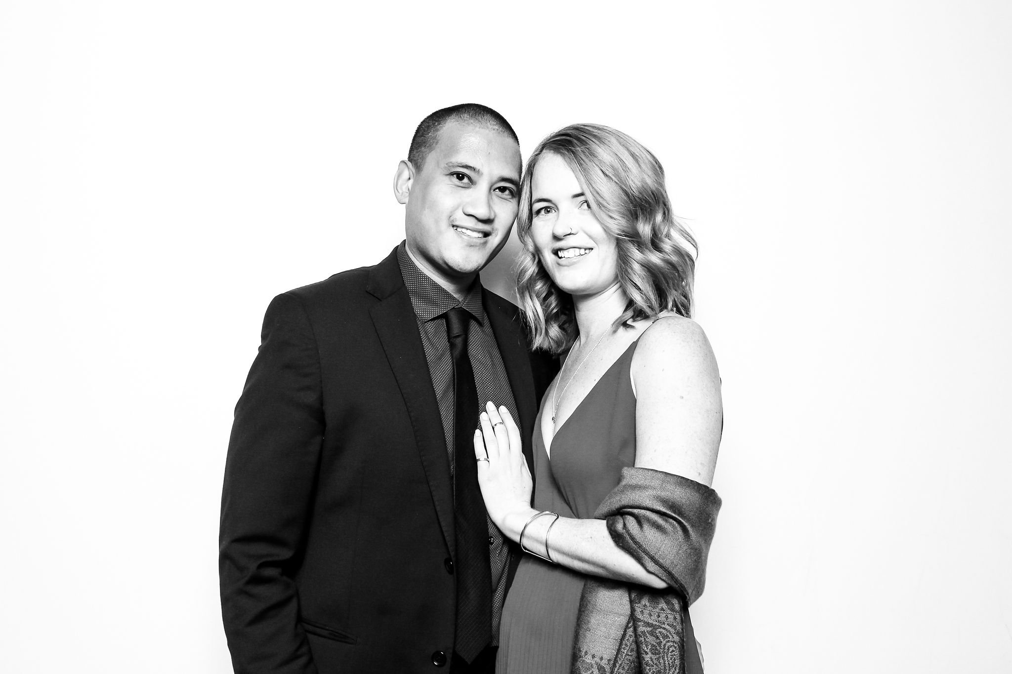 A black and white photo of a couple dressed in formal attire, smiling and posing together against a plain white background.