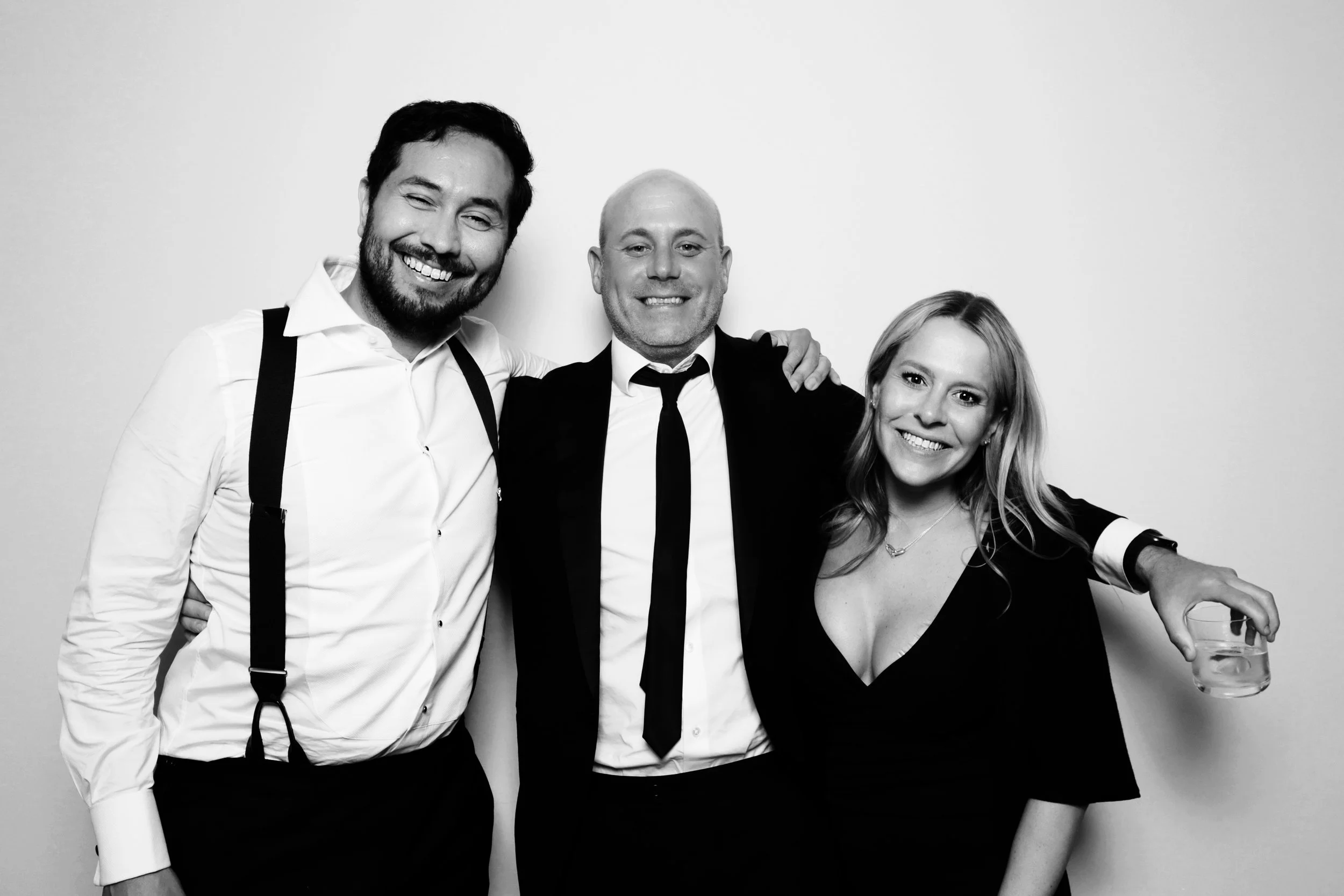 Three people smiling and standing together at a social event, with one woman holding a glass of water.