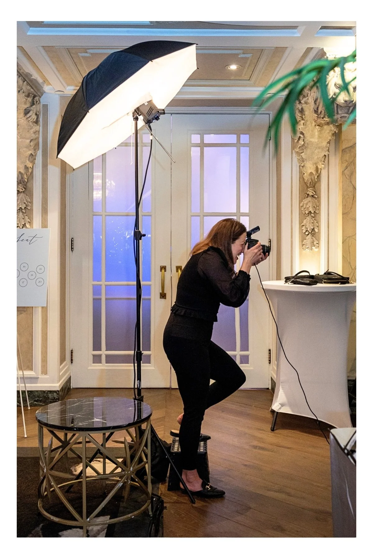 Woman taking a photograph in a room with professional lighting equipment, a table, and large glass doors.