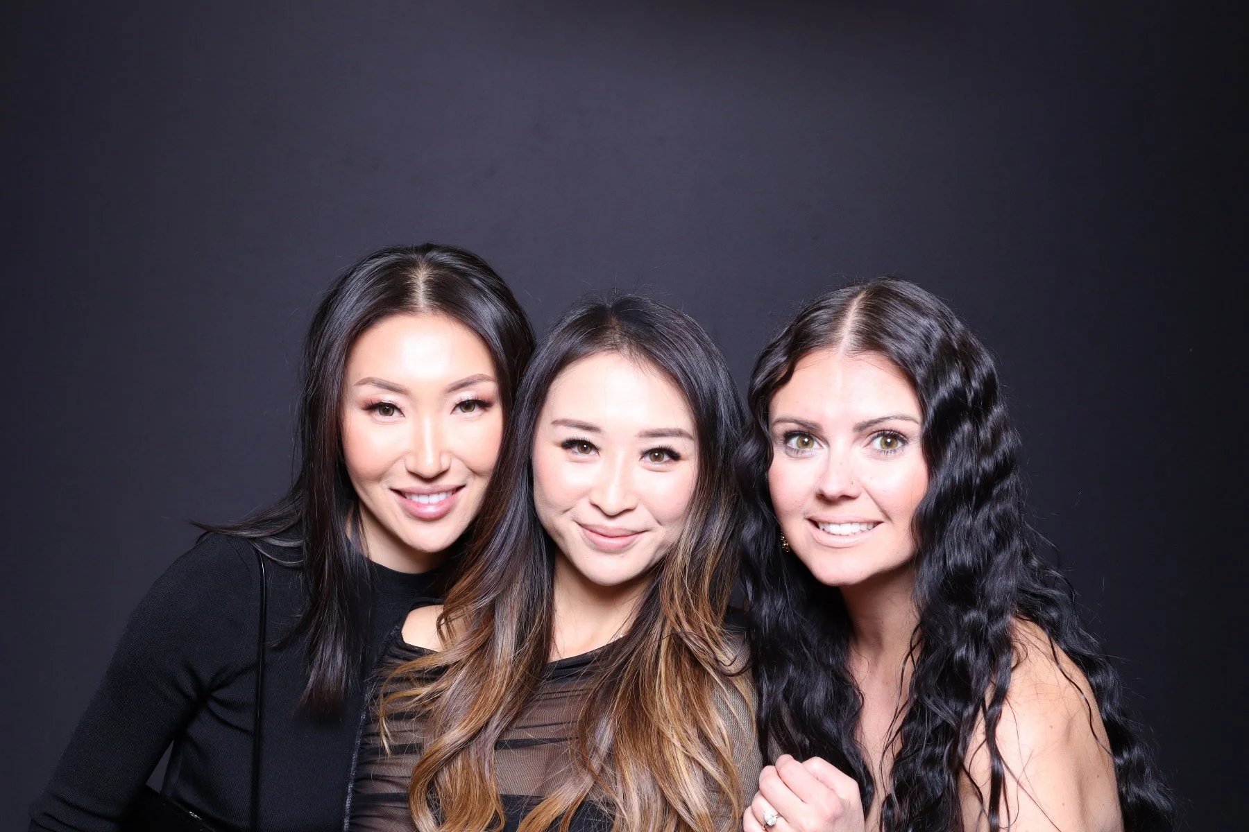 Three women smiling and posing for a photo against a black background.