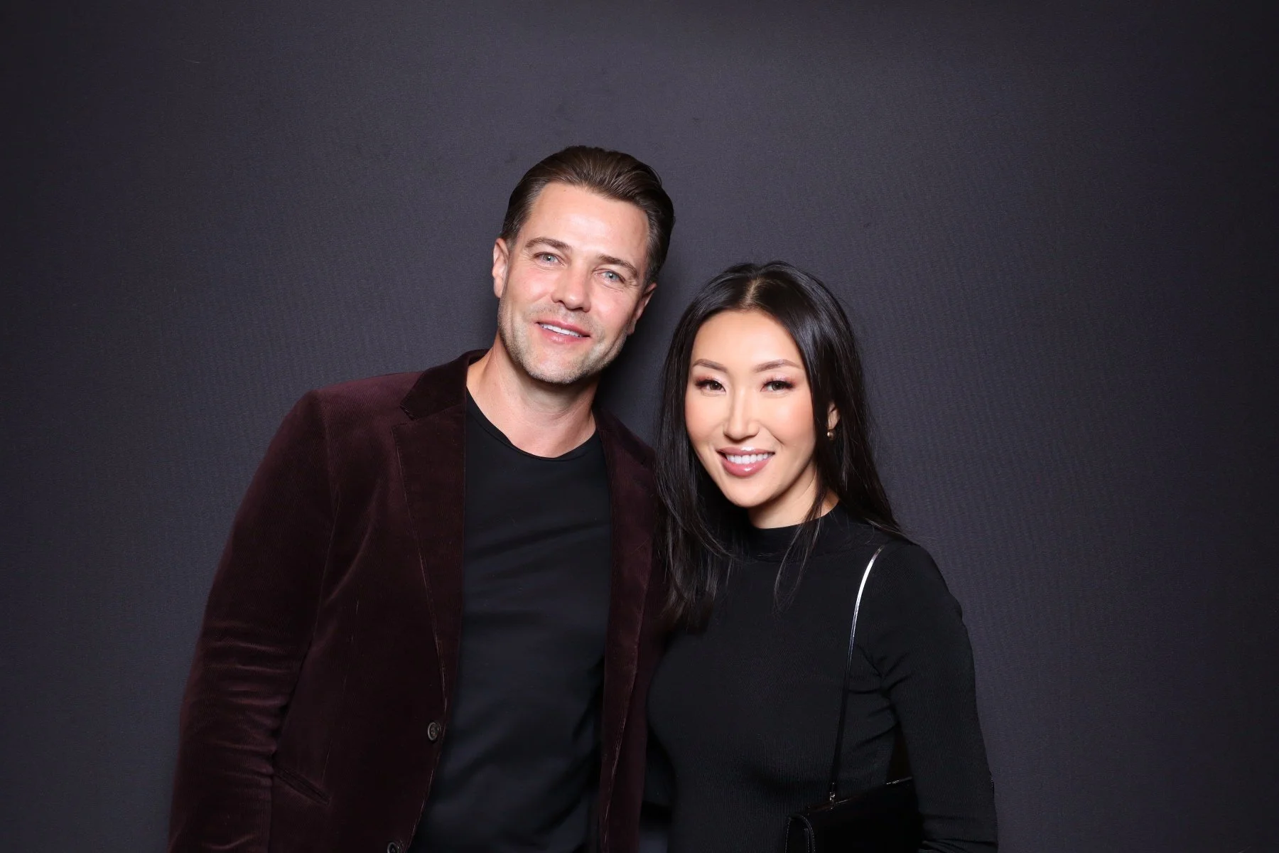 A man and woman standing together against a dark background, smiling at the camera.