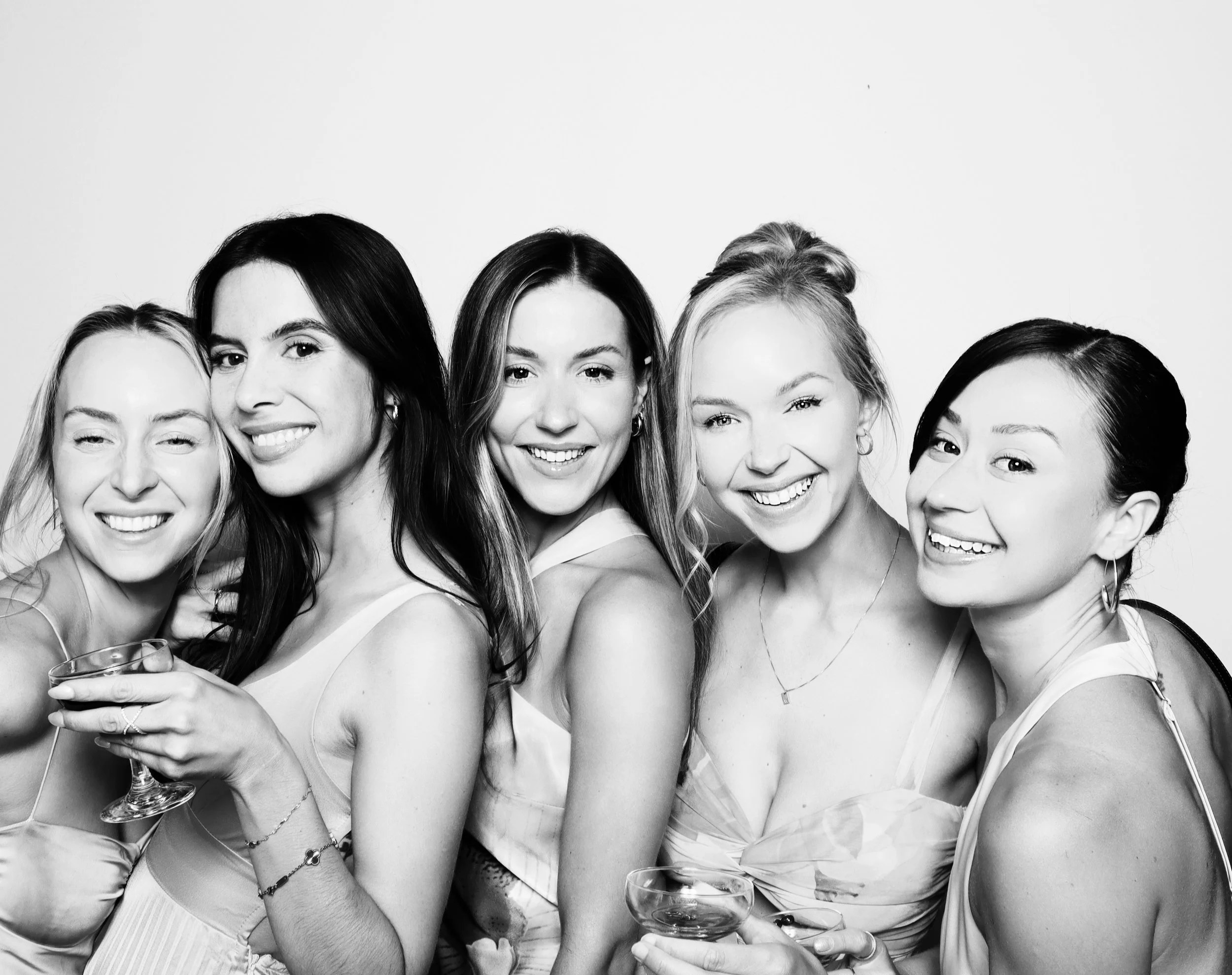 Group of five women smiling and holding drinks in a black-and-white photo.