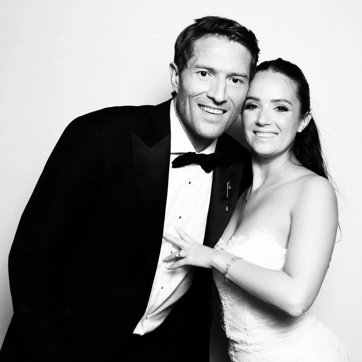 Black and white photo of a smiling man and woman in formal attire, close together, with the woman wearing a wedding dress and the man in a tuxedo.