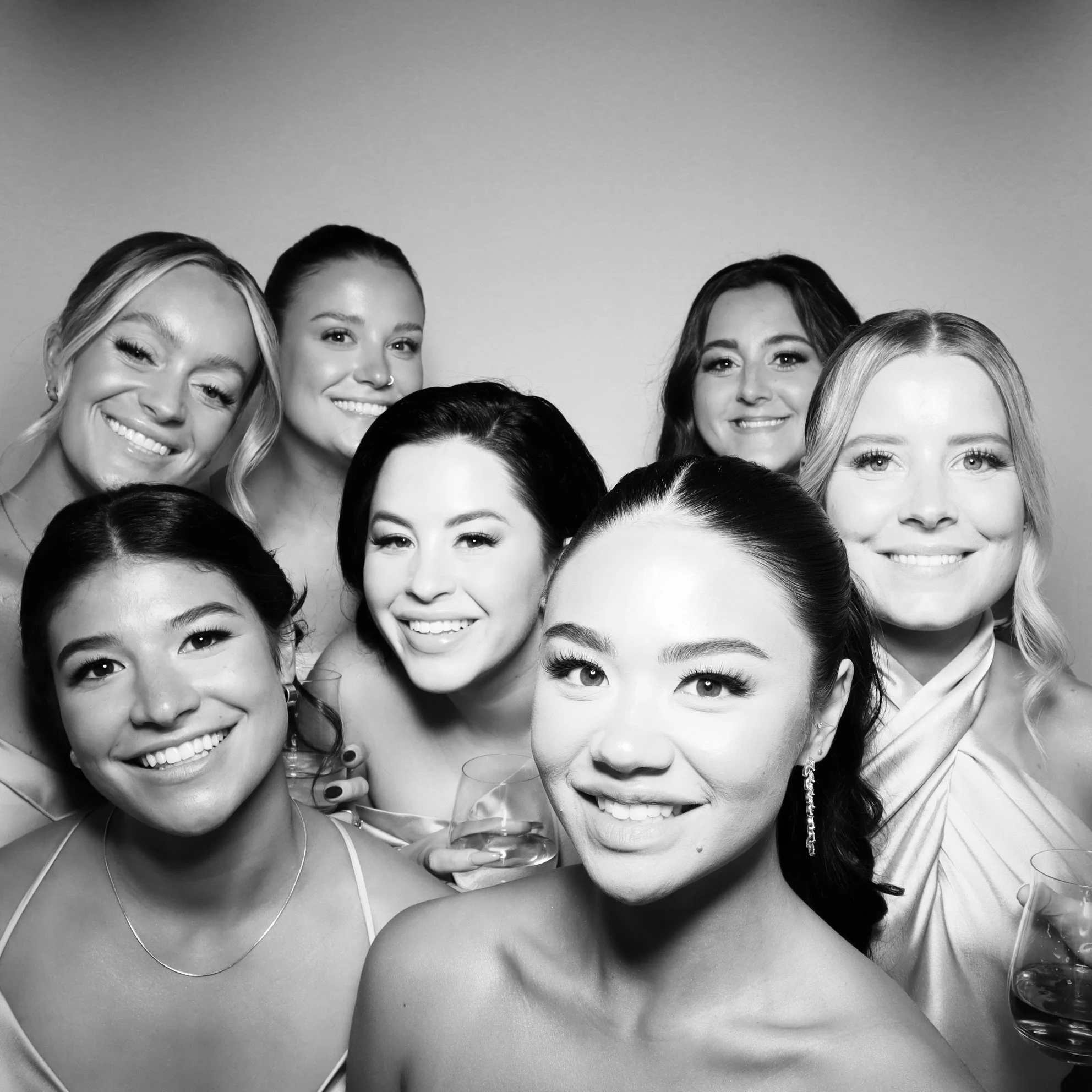 Black and white photo of nine smiling women at a celebration, holding drinks, dressed in elegant attire.