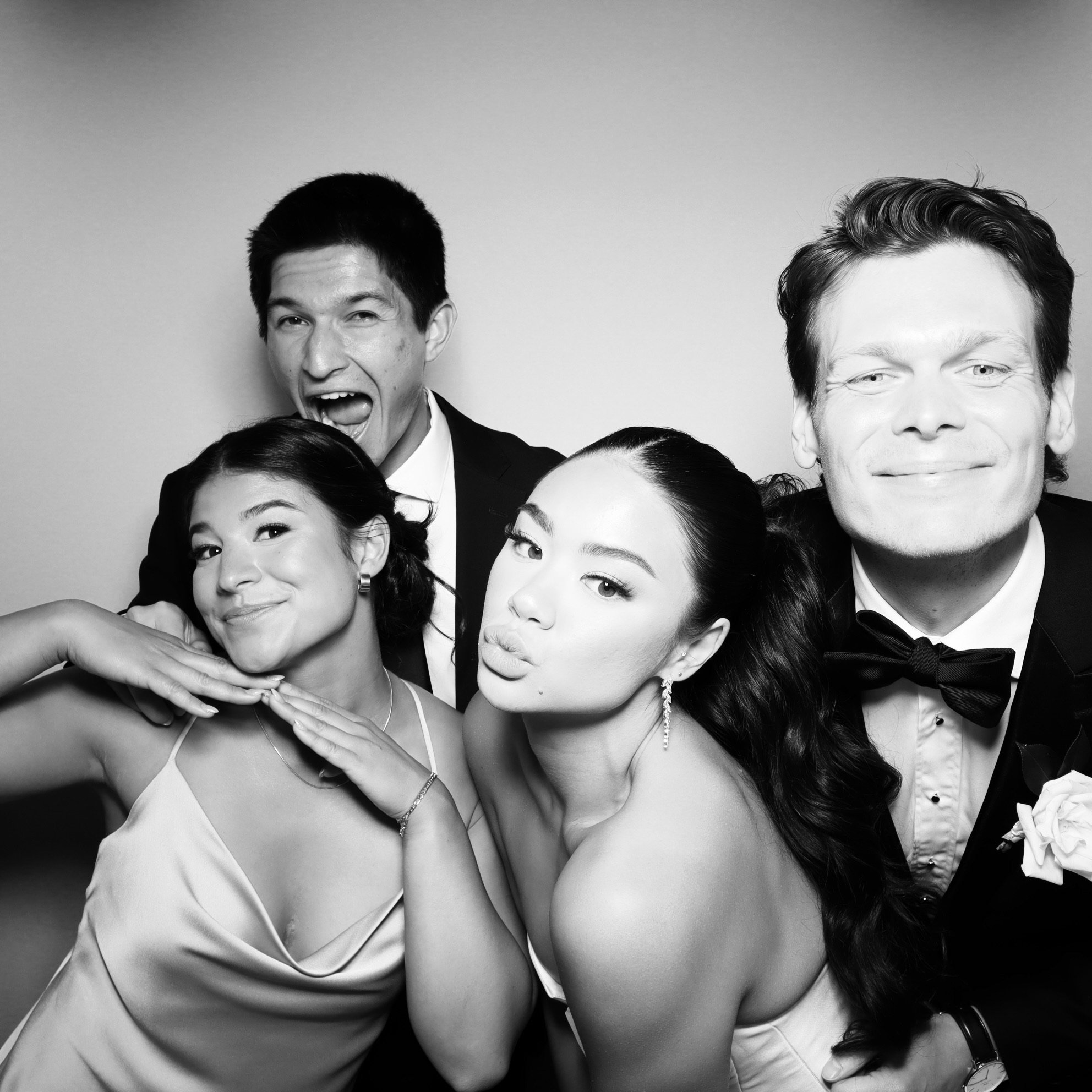 Group of four people dressed formally, posing playfully for a photo in black and white.