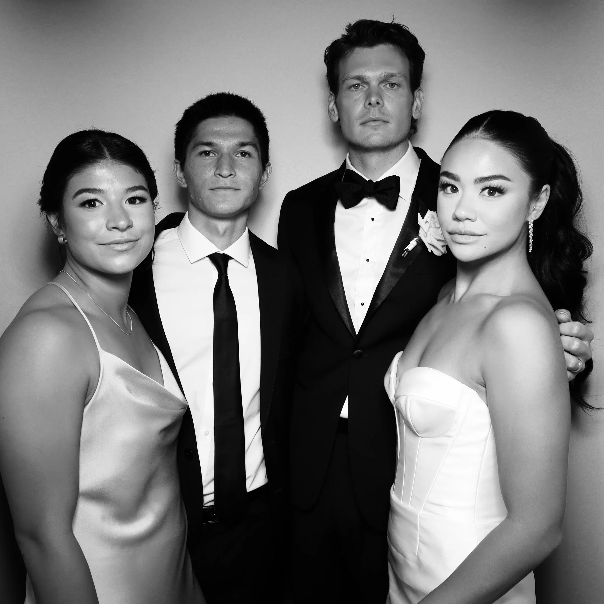 Black and white photo of four elegantly dressed young adults, two women and two men, posing together at formal event, with the women wearing dresses and the men in tuxedos.