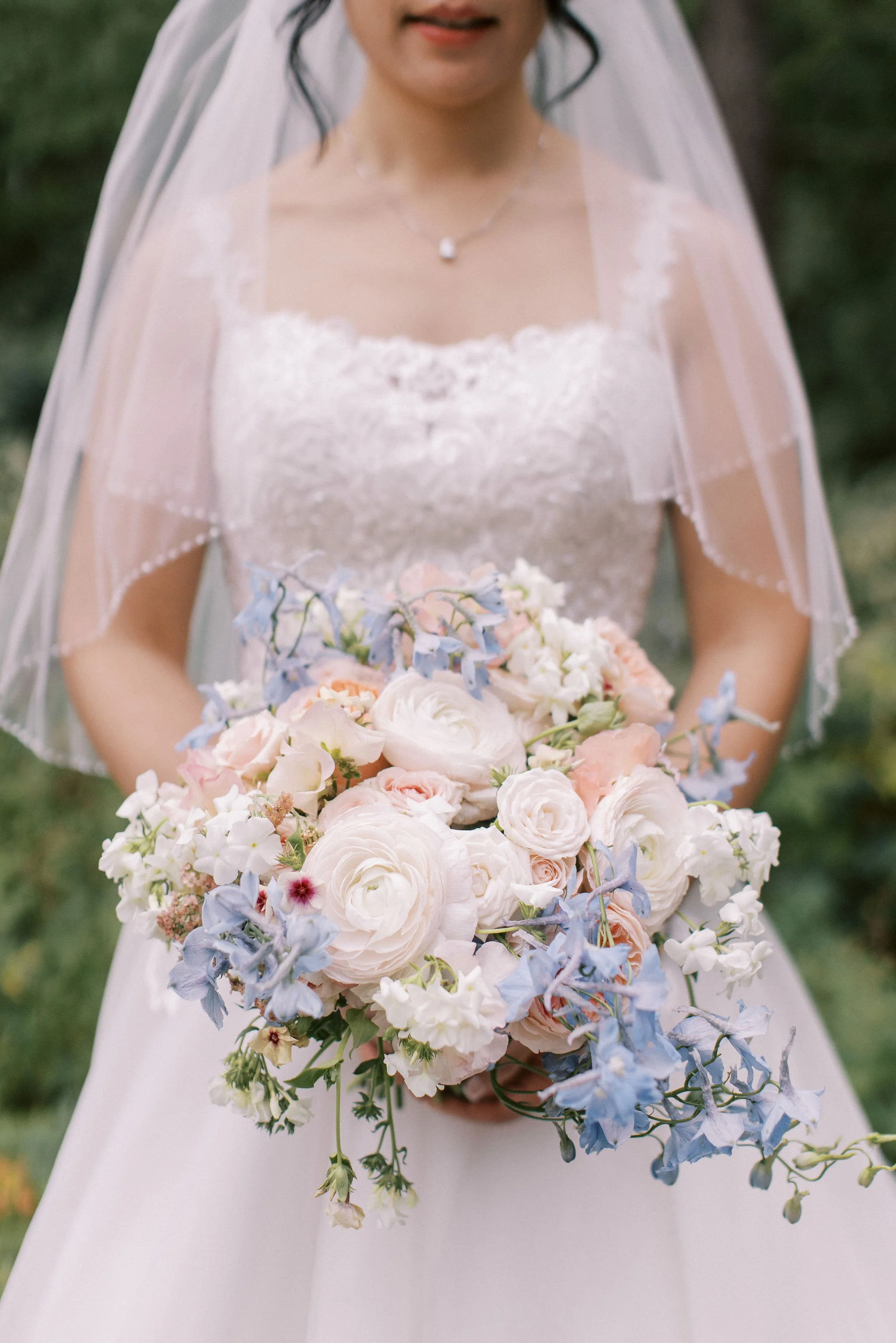 Bride in a wedding dress holding a bouquet of white, pink, and blue flowers.