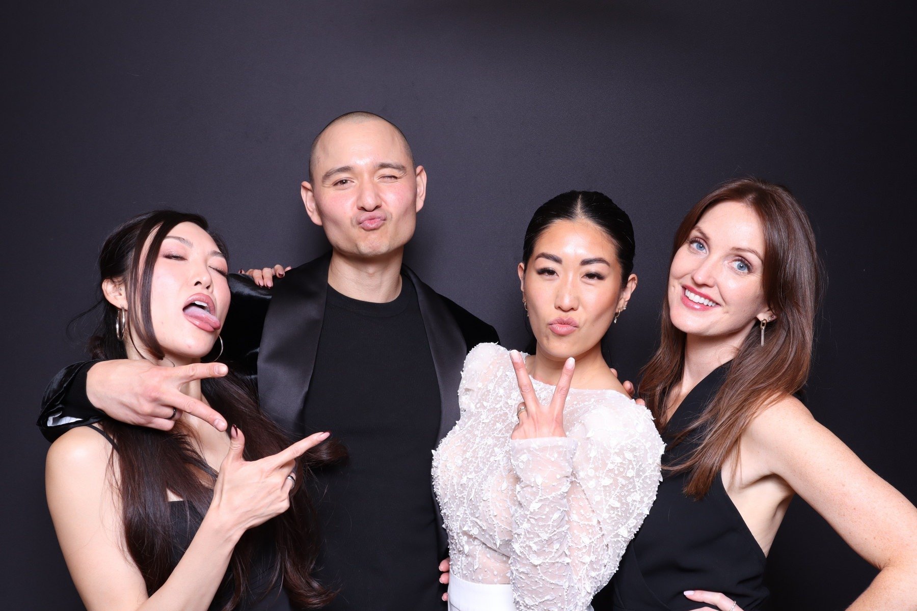 Four diverse young adults posing against a black background, showing playful and confident expressions.