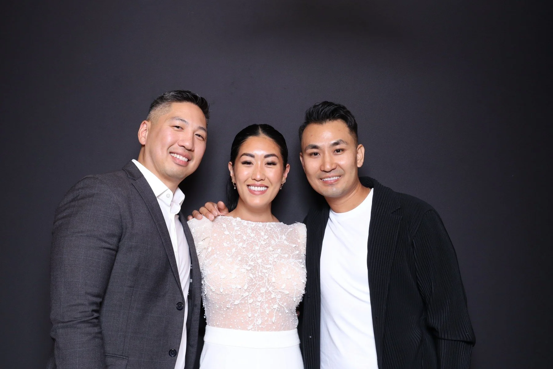 Three people smiling and posing together in front of a black background, with two men and one woman, dressed in semi-formal attire.