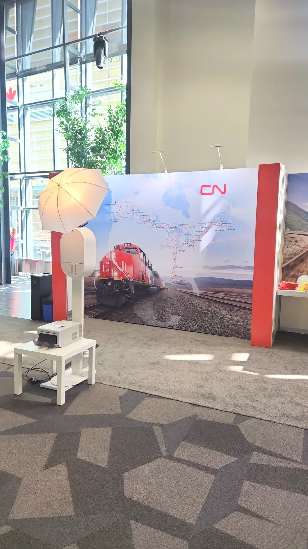 Exhibition booth with CN logo, displaying a large banner of a CN train and map of Canadian rail routes, lit by a floor lamp with a light shade.