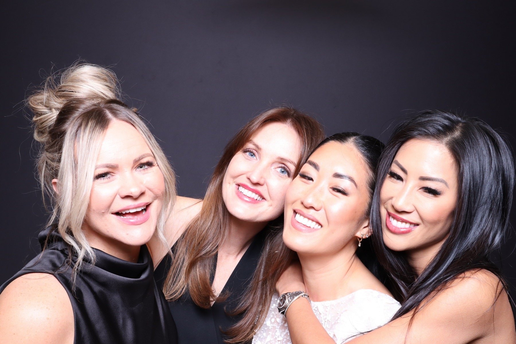 Four women smiling and posing together against a dark background.