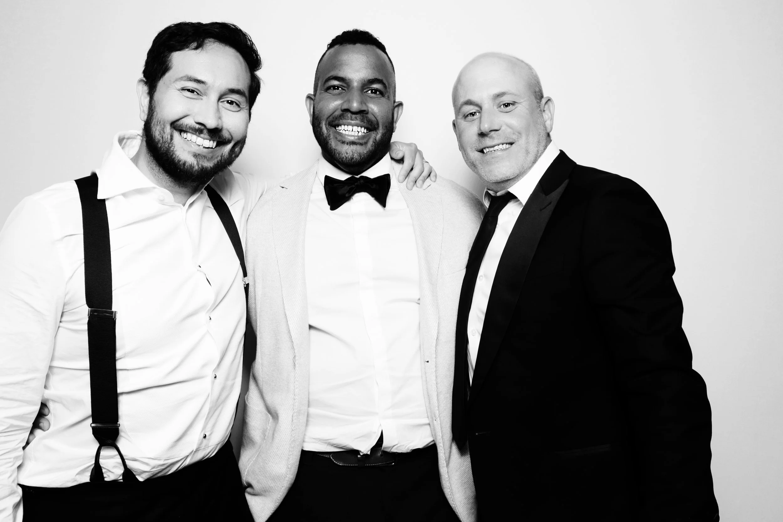 Three men dressed in formal attire, smiling and standing close together, in a black and white photo.
