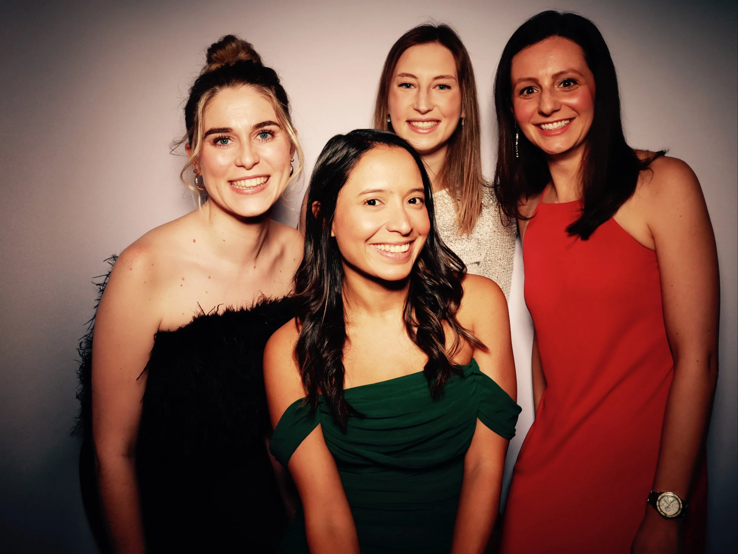 Group of four women smiling in a photo against a plain background, dressed in colorful outfits.
