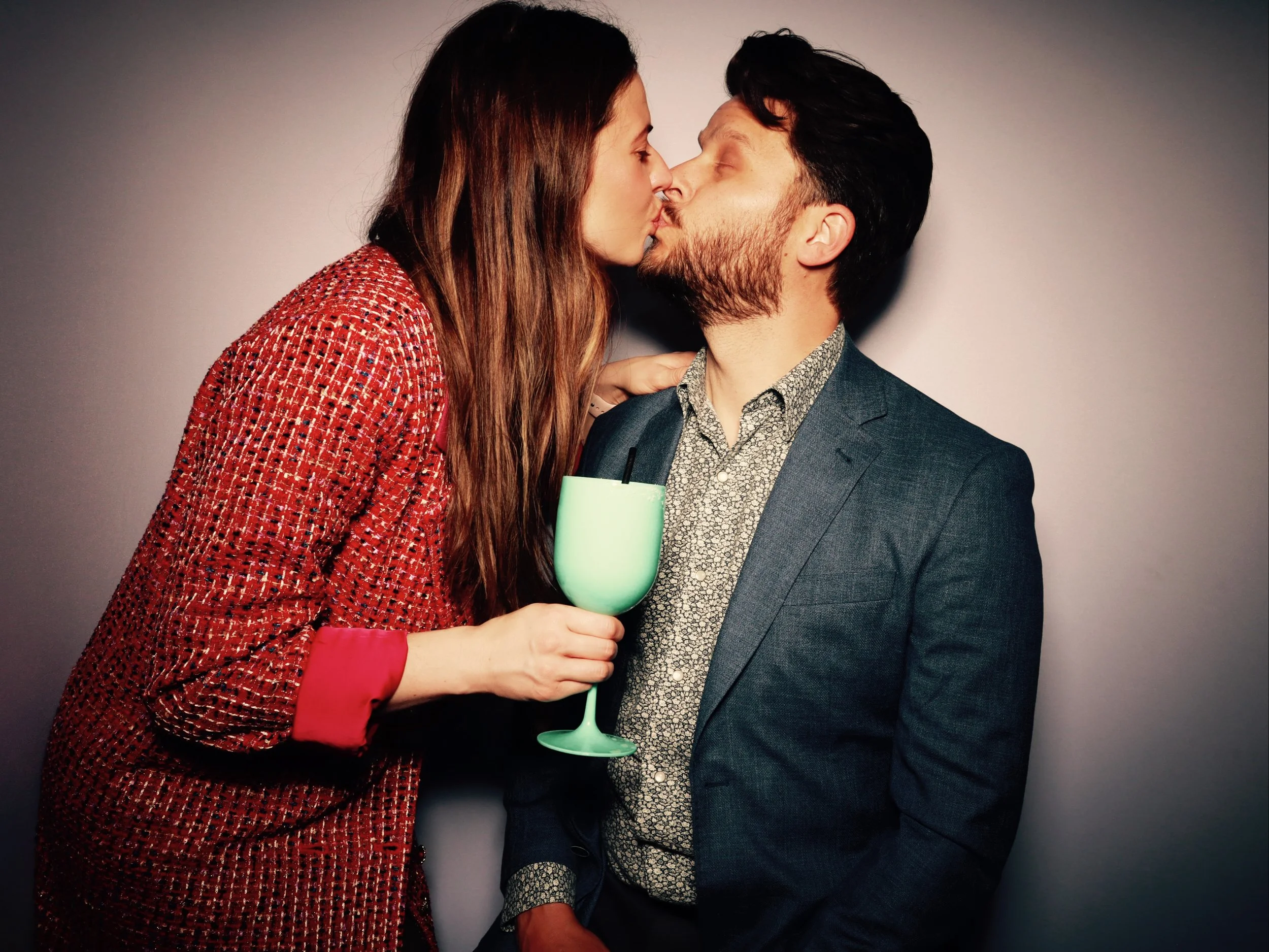 A woman and a man are kissing, with the woman holding a green drink in her hand.