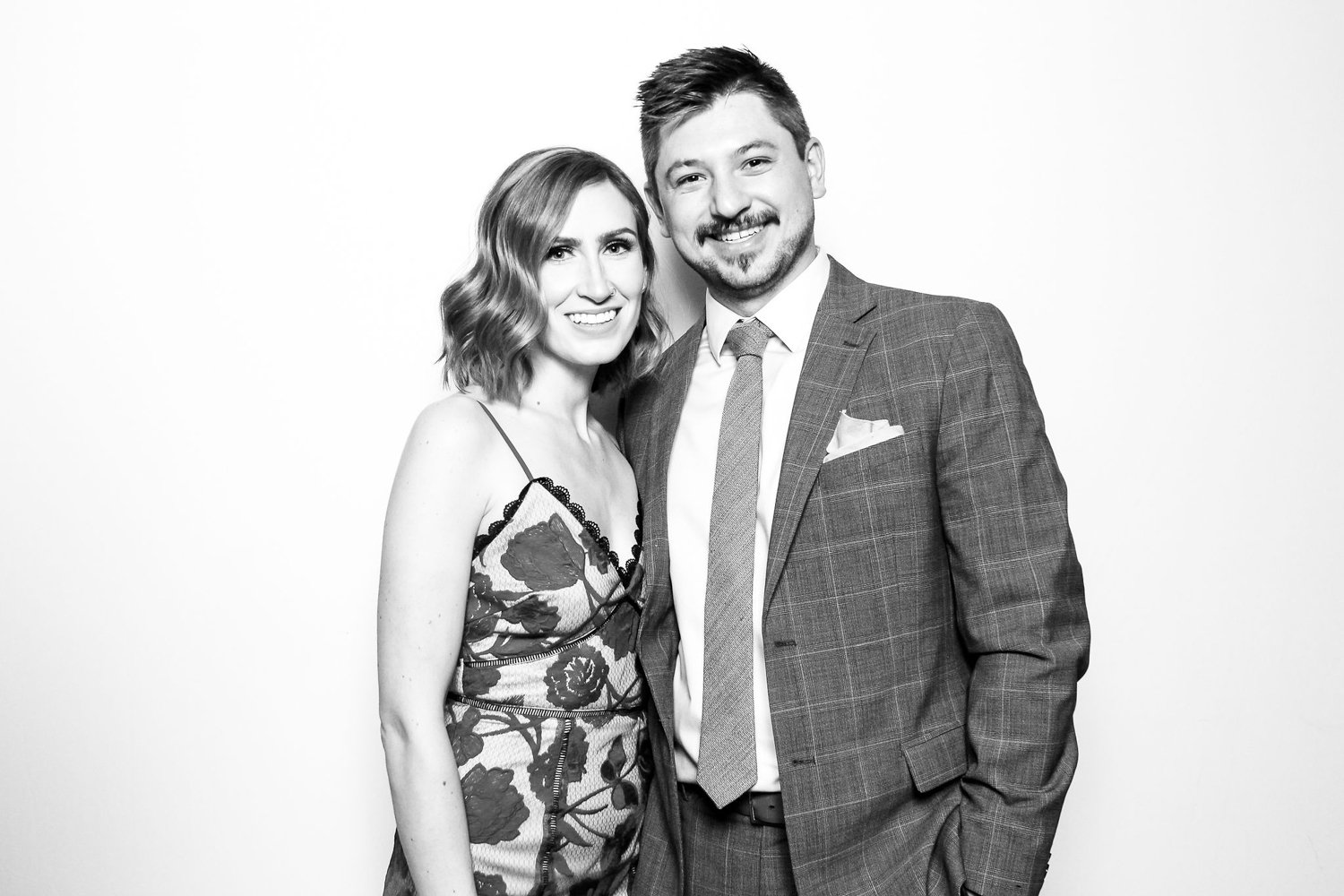 Black and white photo of a smiling woman with wavy hair in a floral dress standing next to a man in a suit and tie.