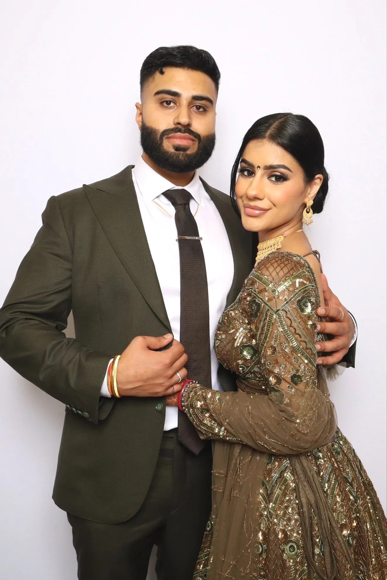 A man in a dark suit and a woman in a traditional Indian dress pose together against a white background.