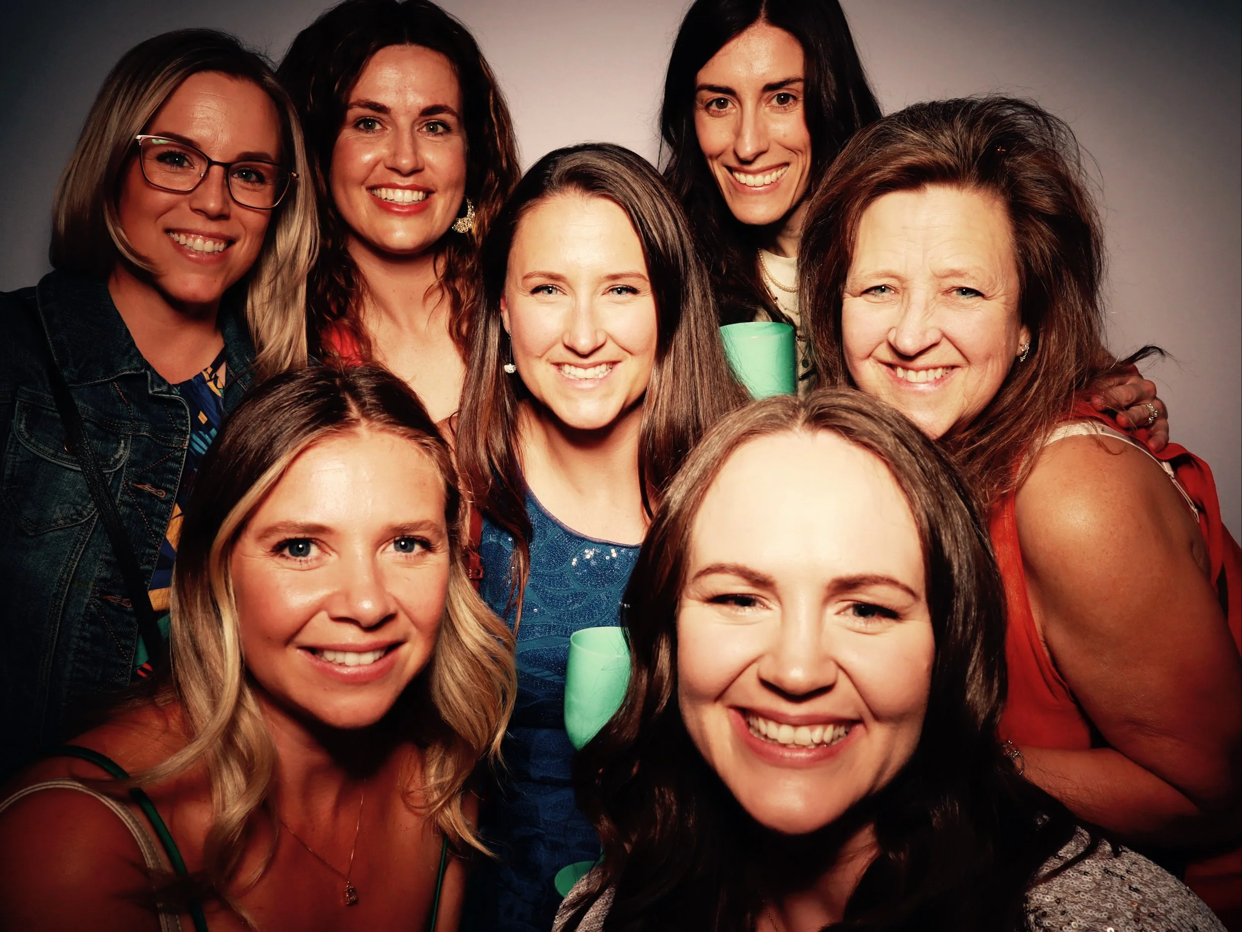 A group of nine smiling women gathered closely together for a photo against a plain background.