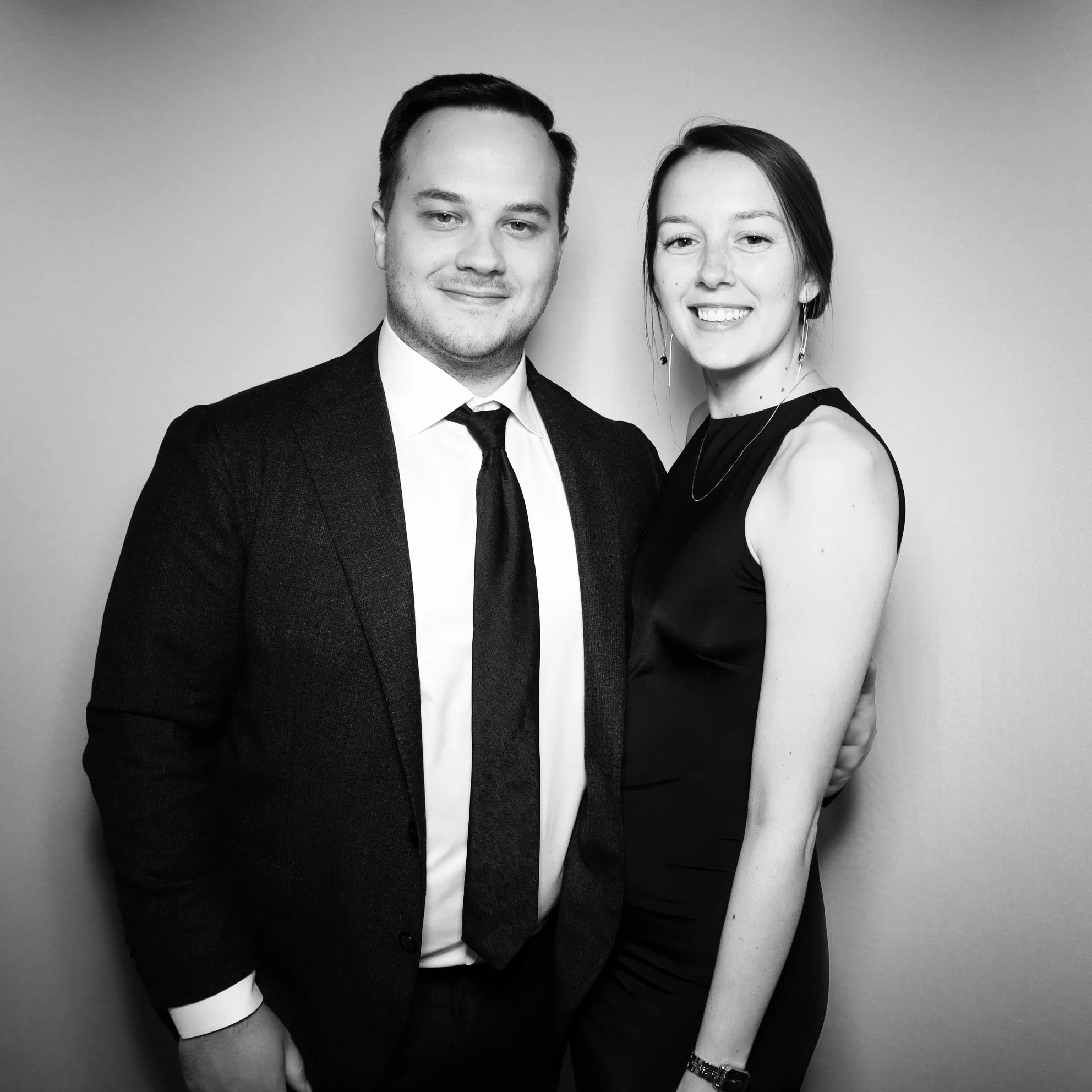 Black and white photo of a man and woman dressed formally, standing close together and smiling at the camera against a plain background.