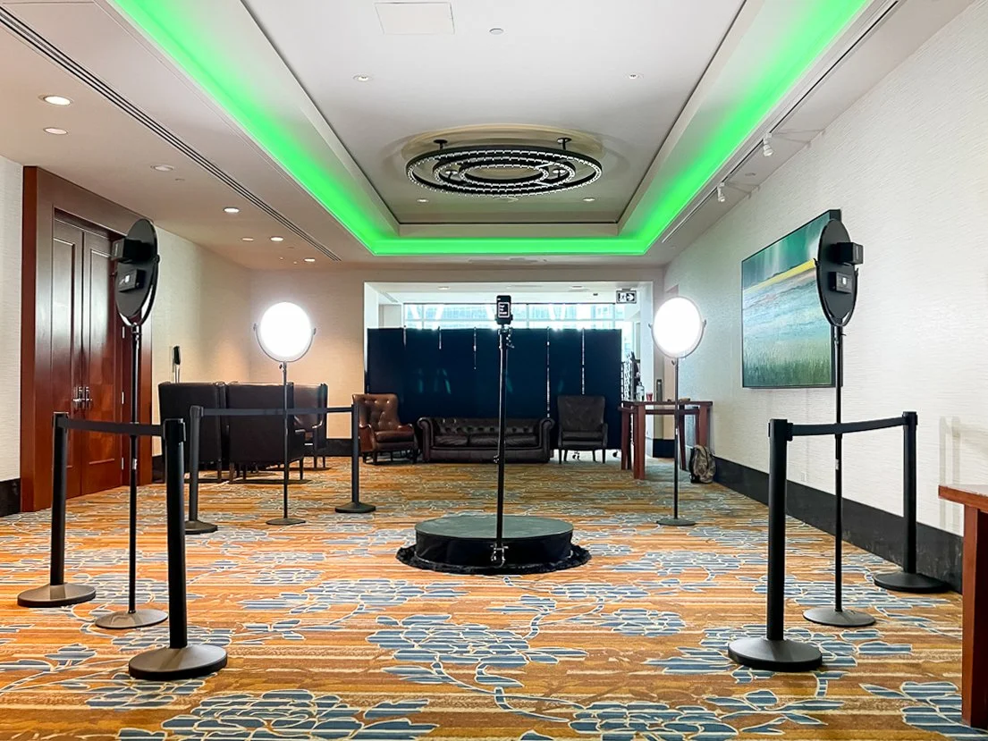 Event setup with ring lights, camera on tripod, and stanchions with ropes in a spacious room.