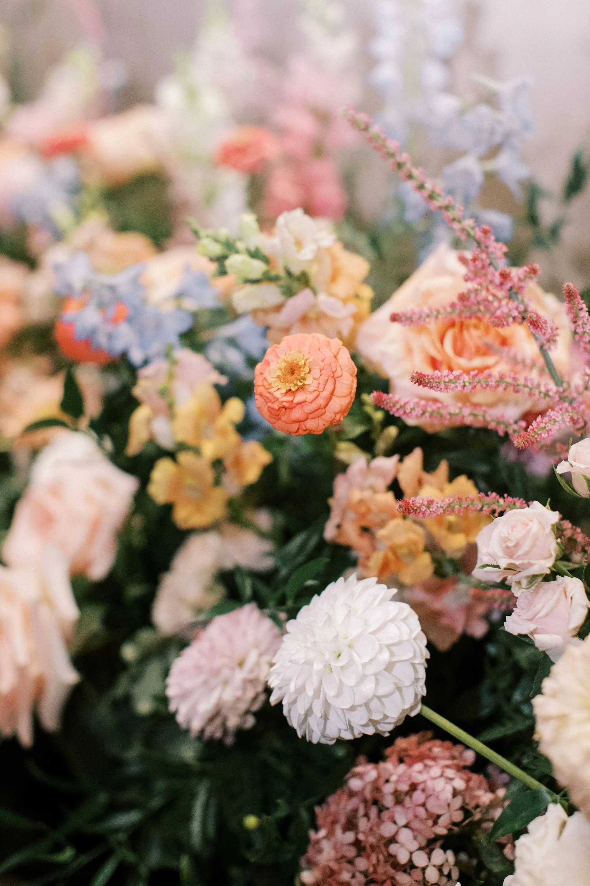 A close-up of a colorful flower bouquet with various pastel-colored flowers including roses, dahlias, and daisies.