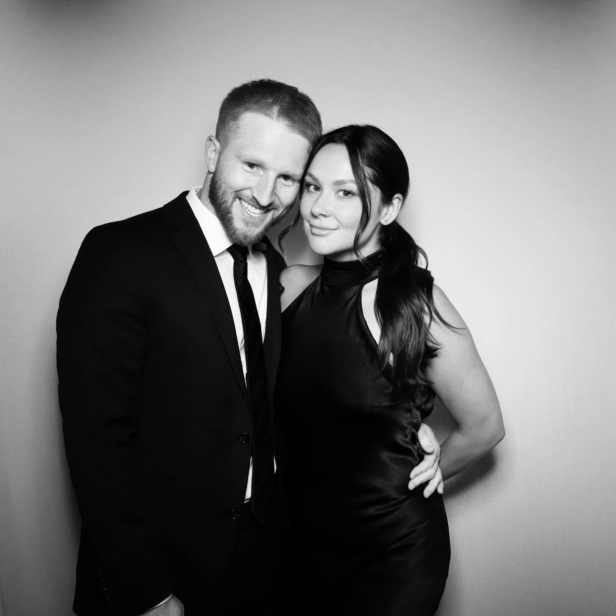 A black and white photo of a man and woman in formal attire smiling and posing together against a plain background.