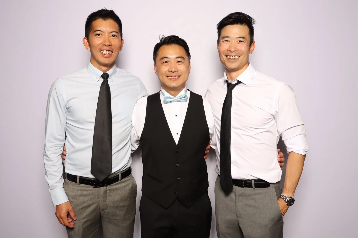Three men dressed in formal attire standing together and smiling at the camera against a plain background.