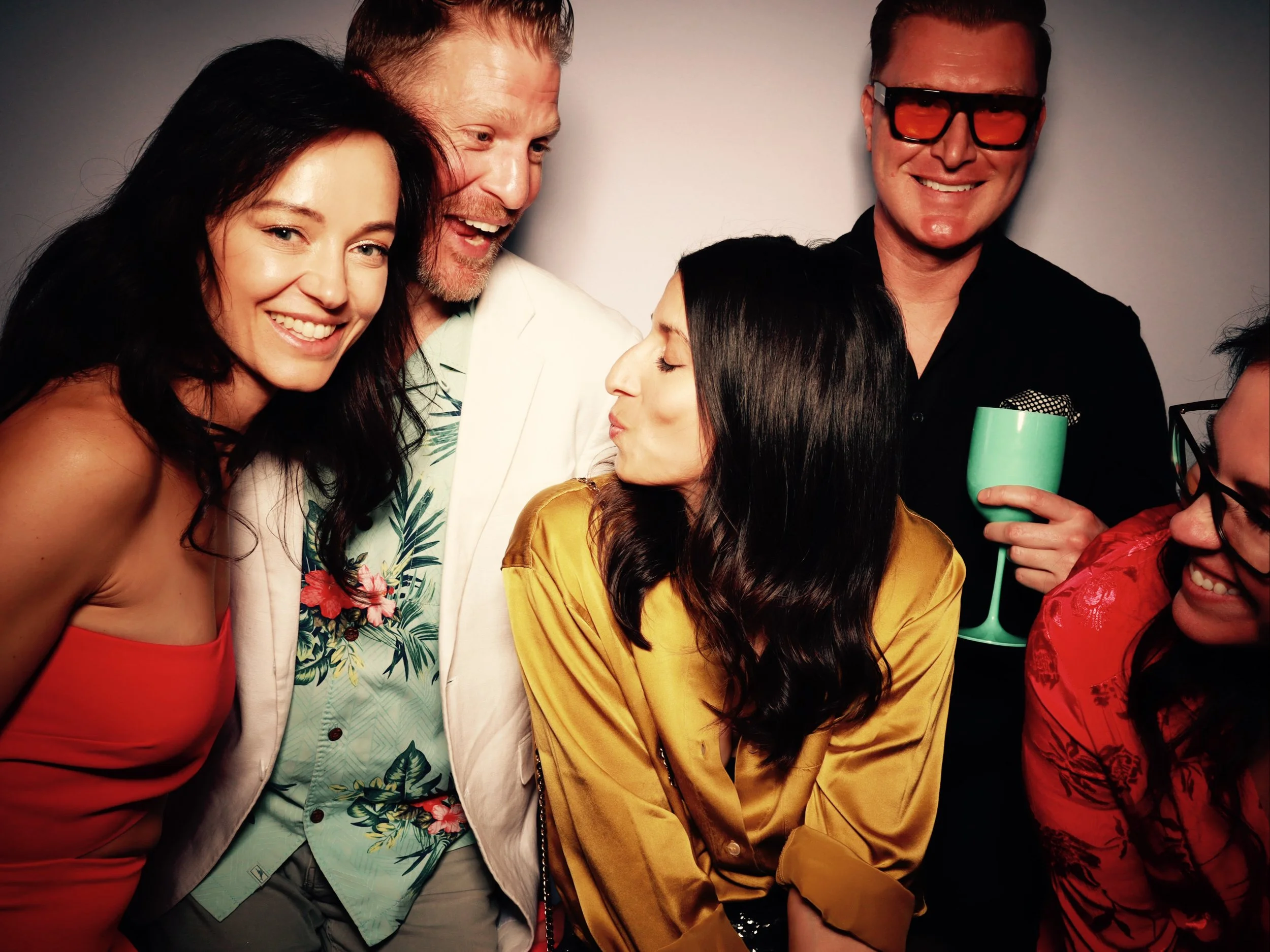 A group of five people smiling and posing together at a party, with one person holding a drink.
