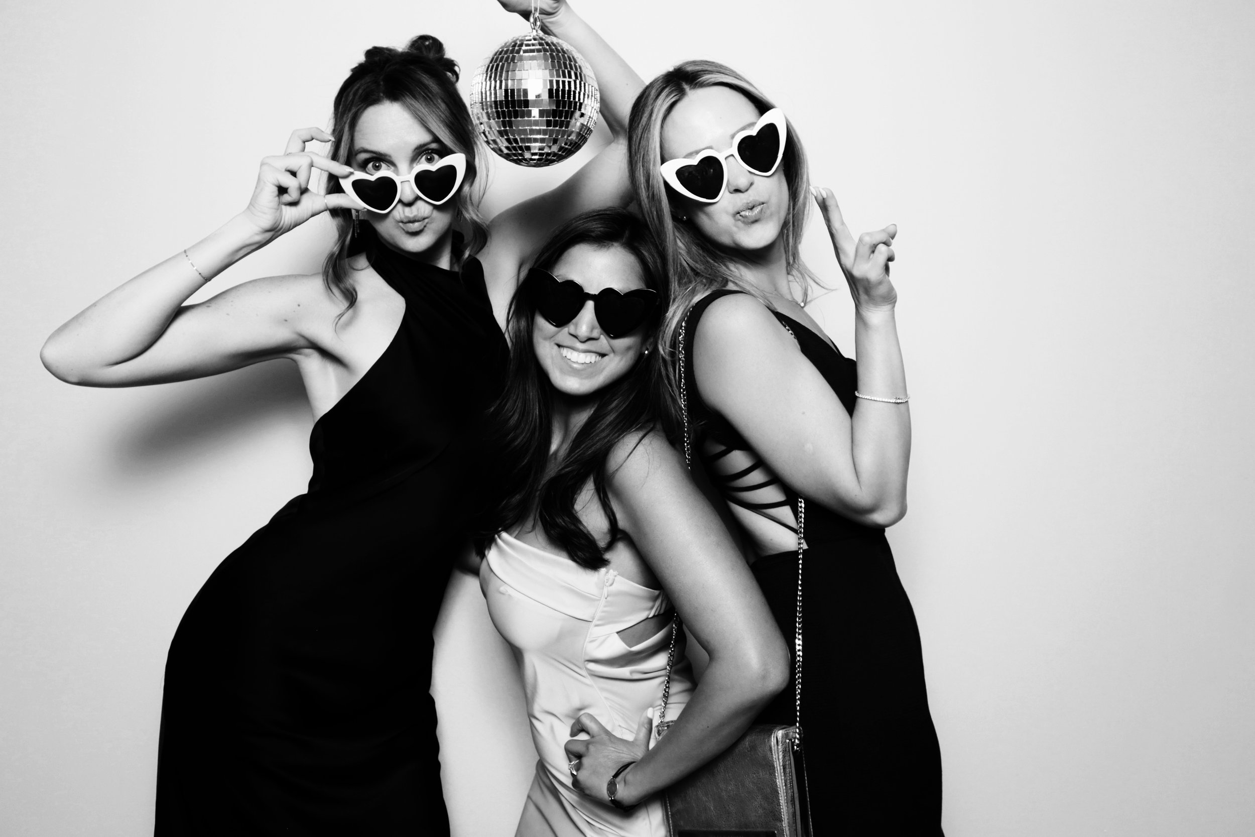 Three women at a party wearing sunglasses, one holding a disco ball, smiling and posing for the camera, black and white photo.