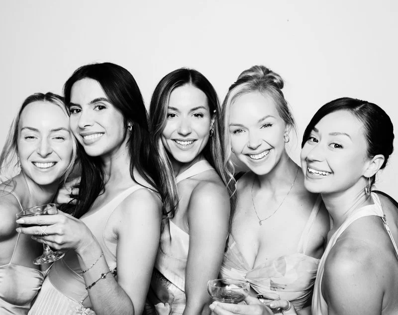 Five young women smiling and holding drinks at a party or celebration.