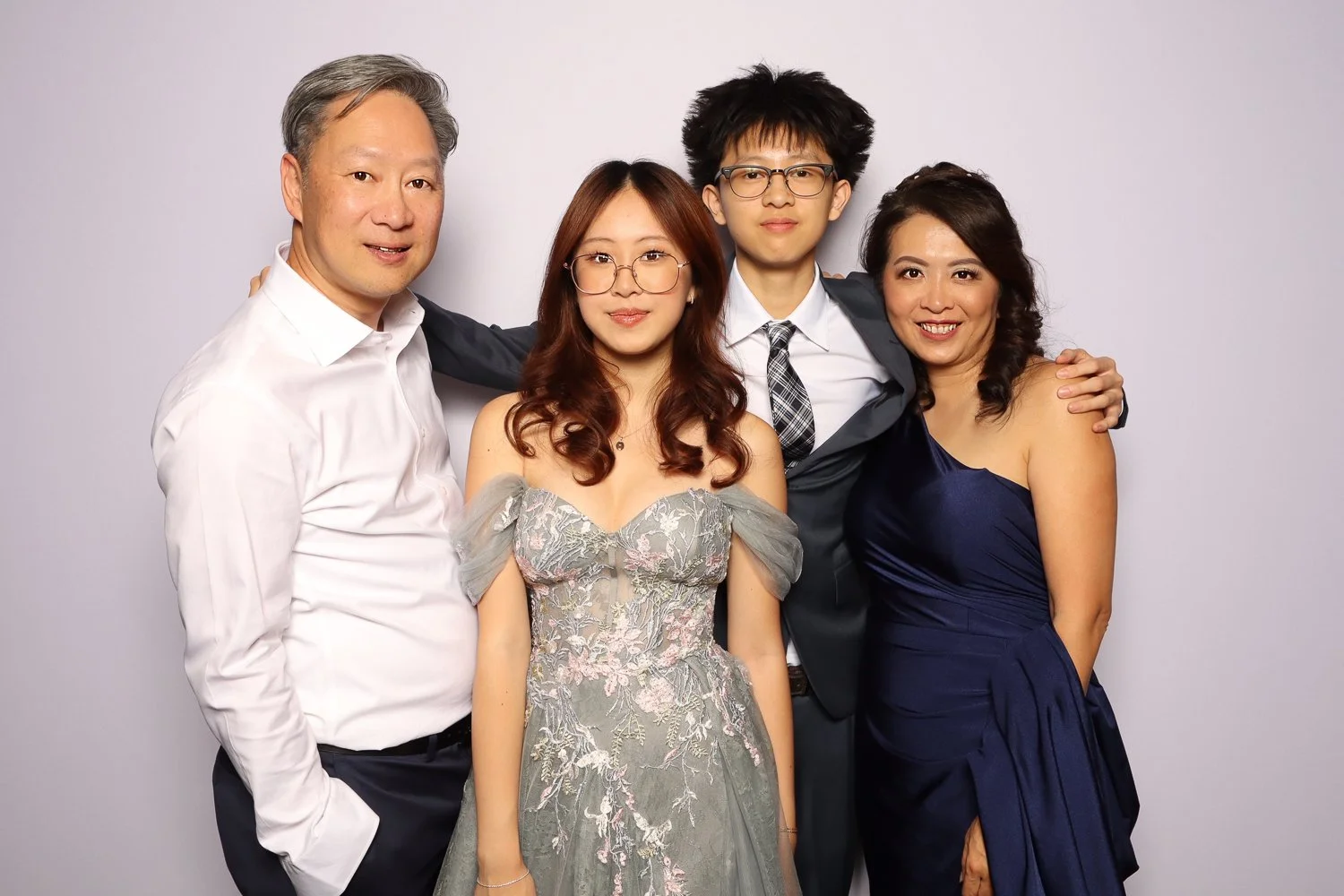 Group of four people, two men and two women, posing together at a formal event, dressed in elegant attire, smiling against a plain background.