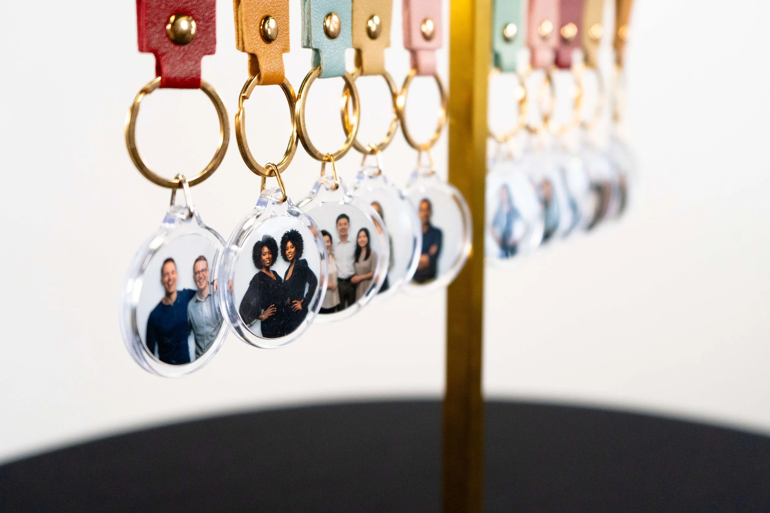Keychain display with multiple acrylic keychains holding group photos of diverse people, attached to colorful straps on a stand.