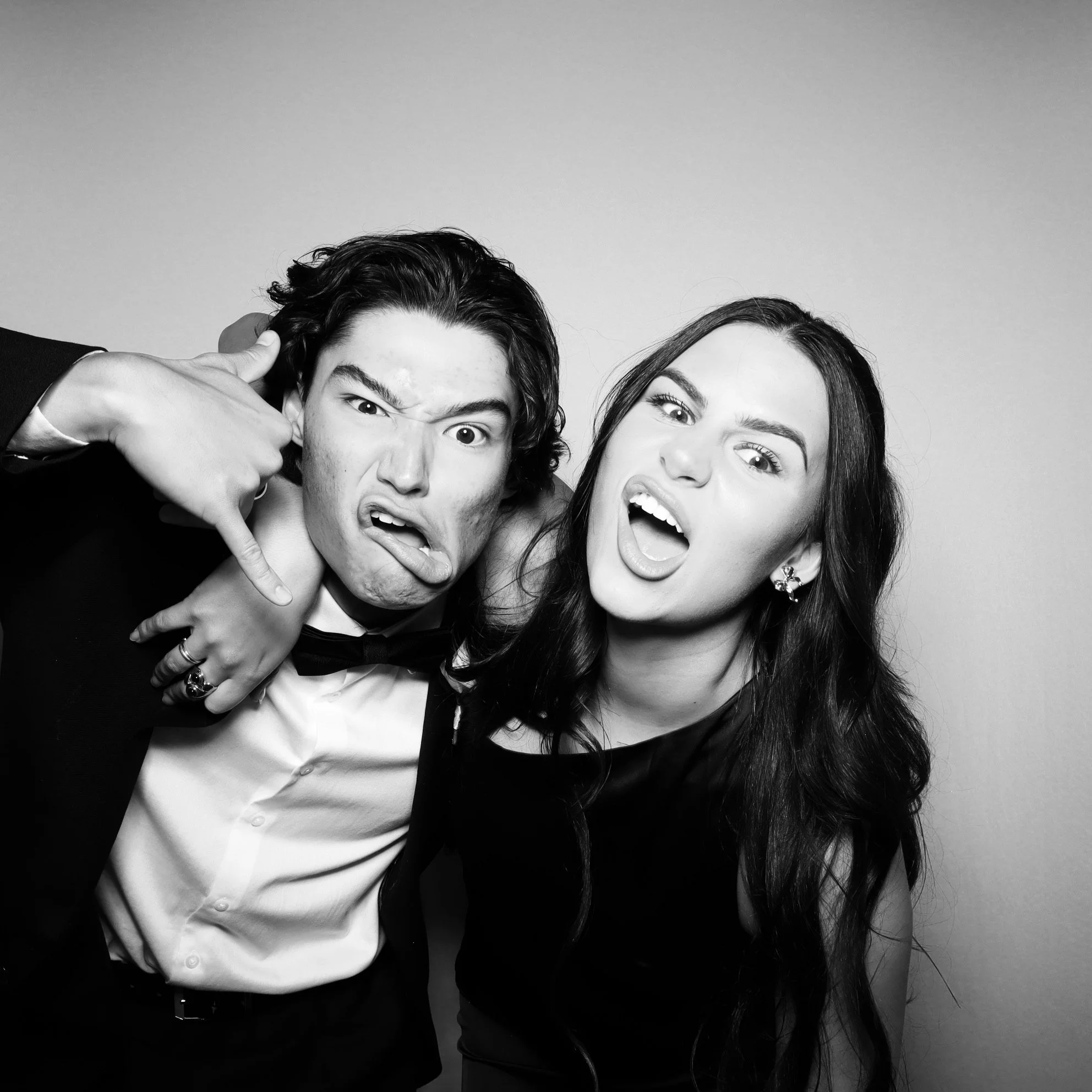 Black and white photo of a young man and woman making silly faces, with the man holding his hand to his ear in a 'call me' gesture, both showing expressive emotions against a plain background.