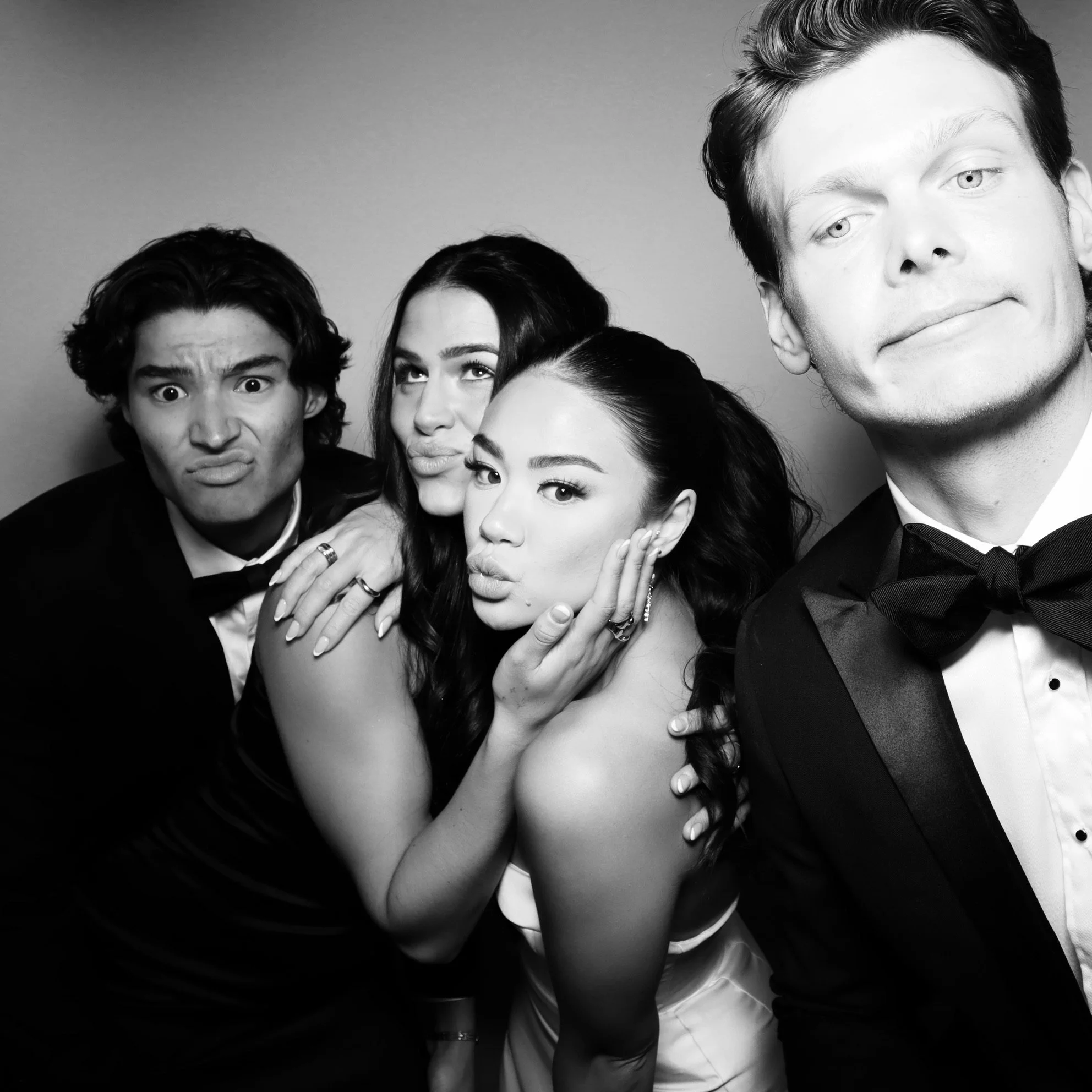 Black and white photo of four young adults dressed in formal attire making playful expressions and poses.