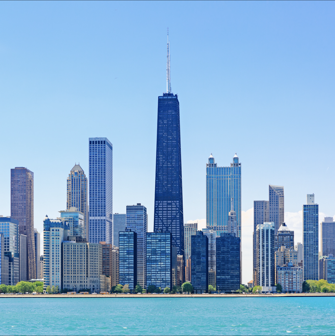 Skyline of downtown Chicago with Lake Michigan in the foreground, featuring the Willis Tower (formerly Sears Tower) under a clear blue sky.
