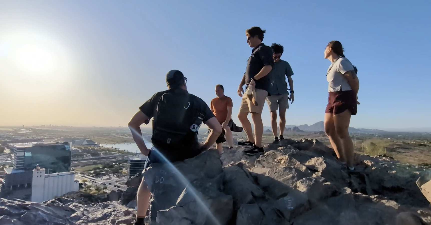 Group of SEJ conference attendees standing on rocks on a hilltop with a cityscape and mountains in the background during sunset.