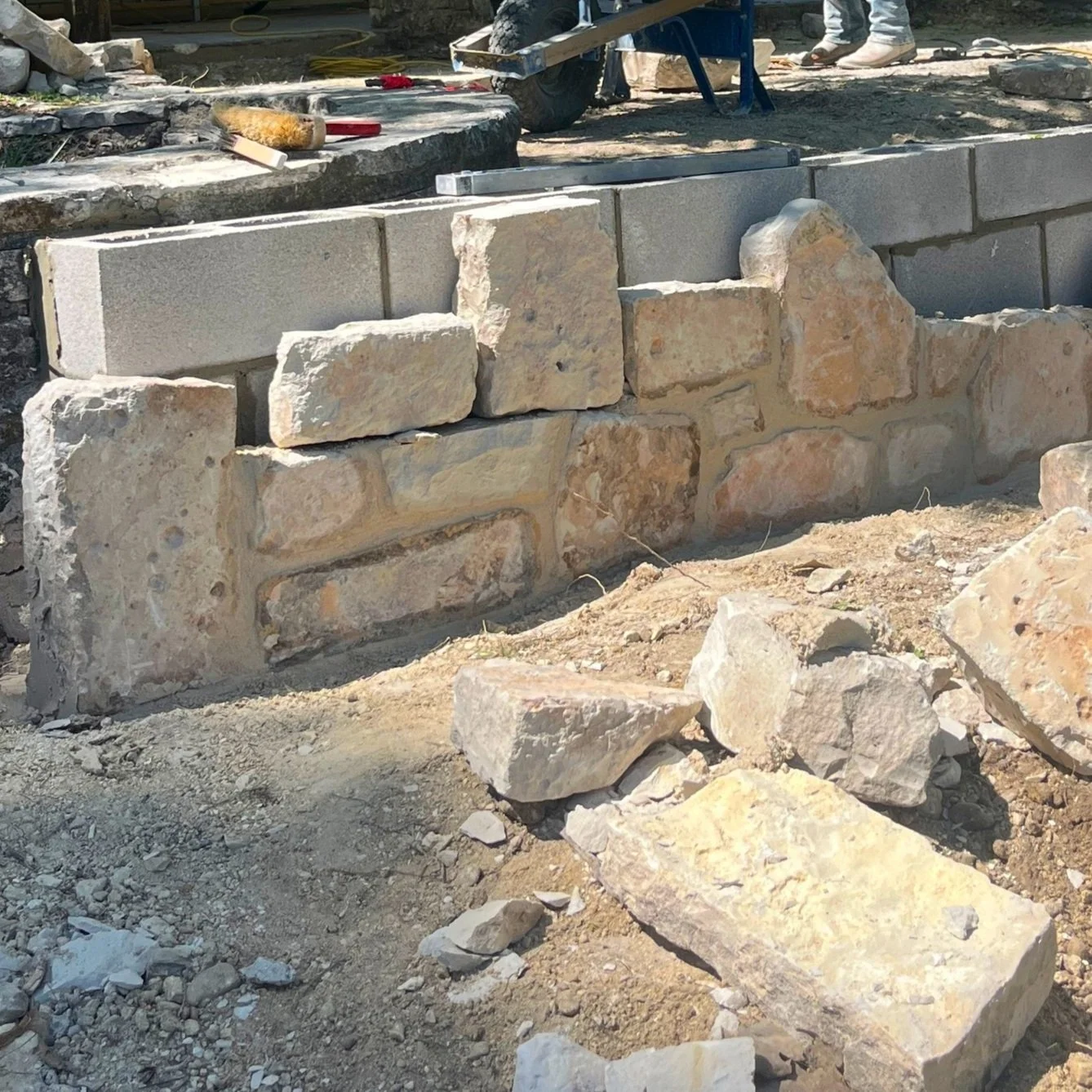 Construction site with a partially built stone wall and tools in the background.