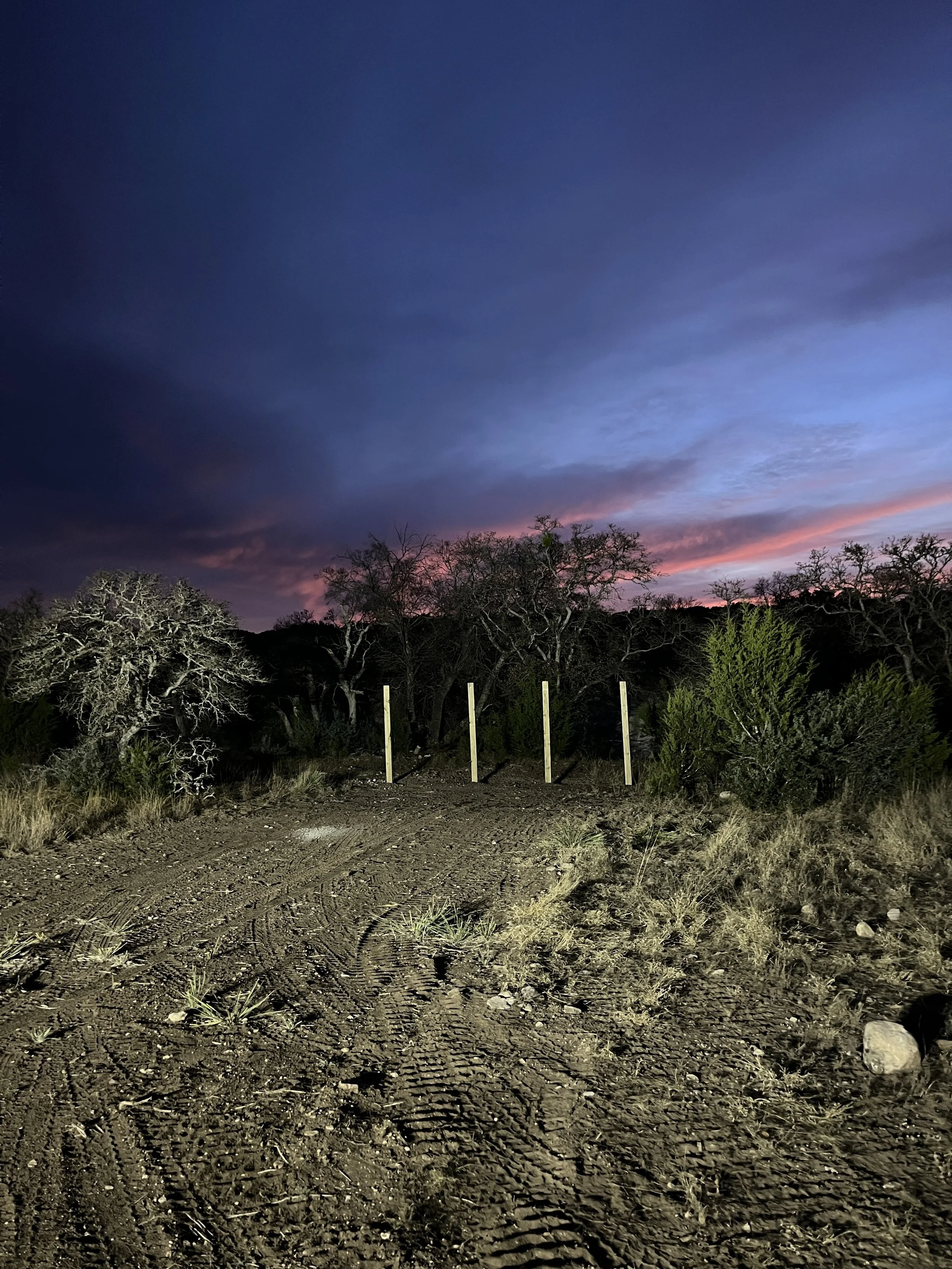 Dirt trail at dusk with sunset sky and leafless trees in the background.