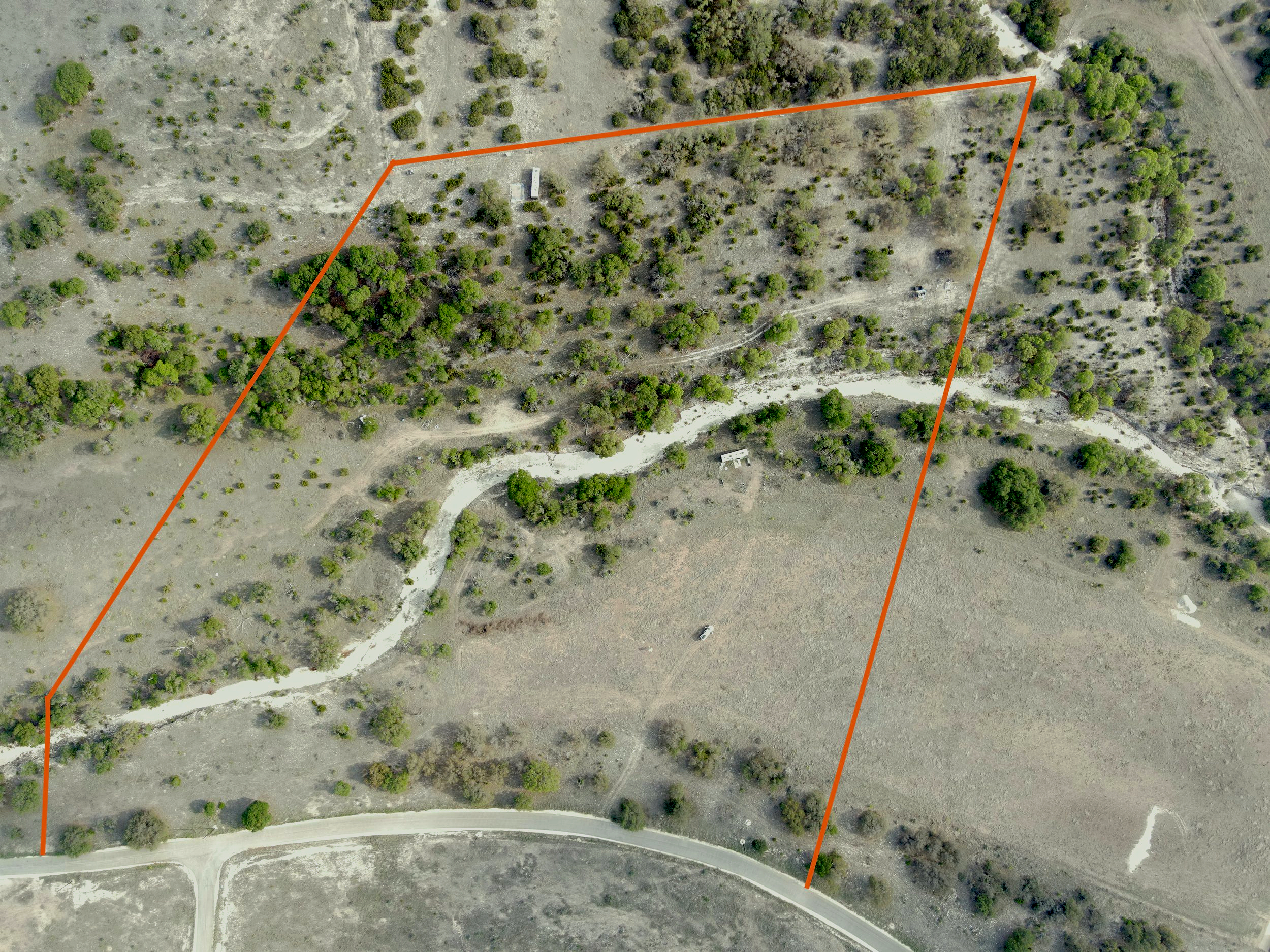 Aerial view of a piece of land with trees, a winding dirt road, and some small structures, outlined by an orange border.