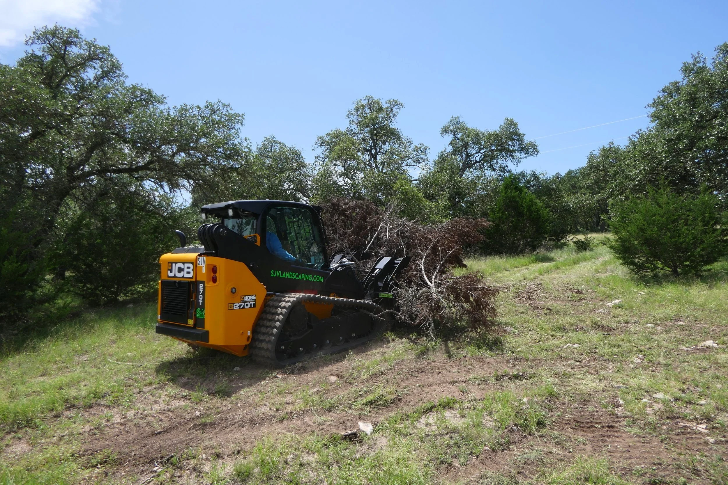 A small tracked excavator with a yellow and black body, working on clearing a patch of land with trees in the background.